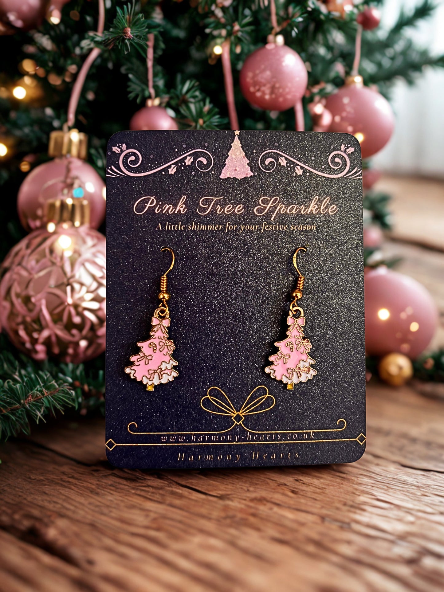 Pink tree-shaped earrings on a 'Pink Tree Sparkle' card with Christmas decorations in the background.