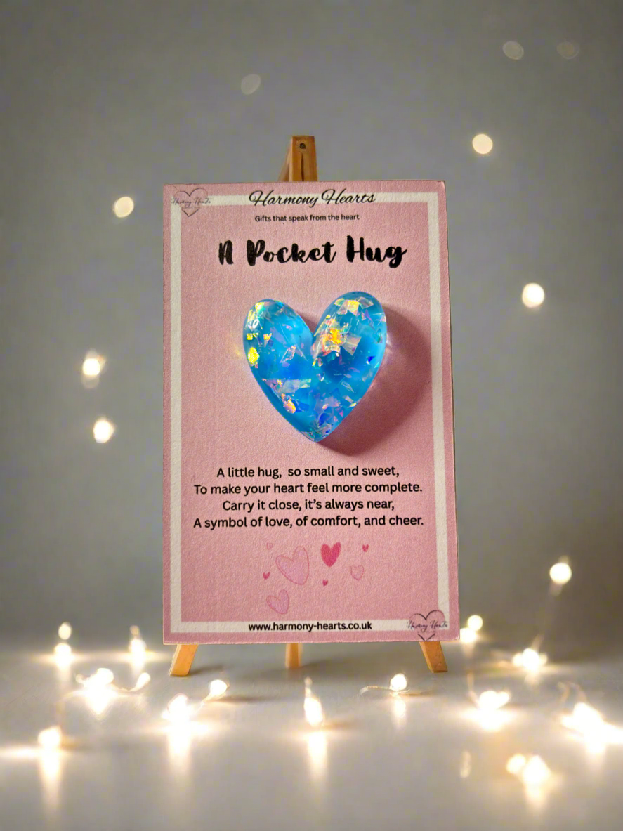 Heart-shaped blue plush toy on a pink card with text, placed on a small easel against a soft light background.