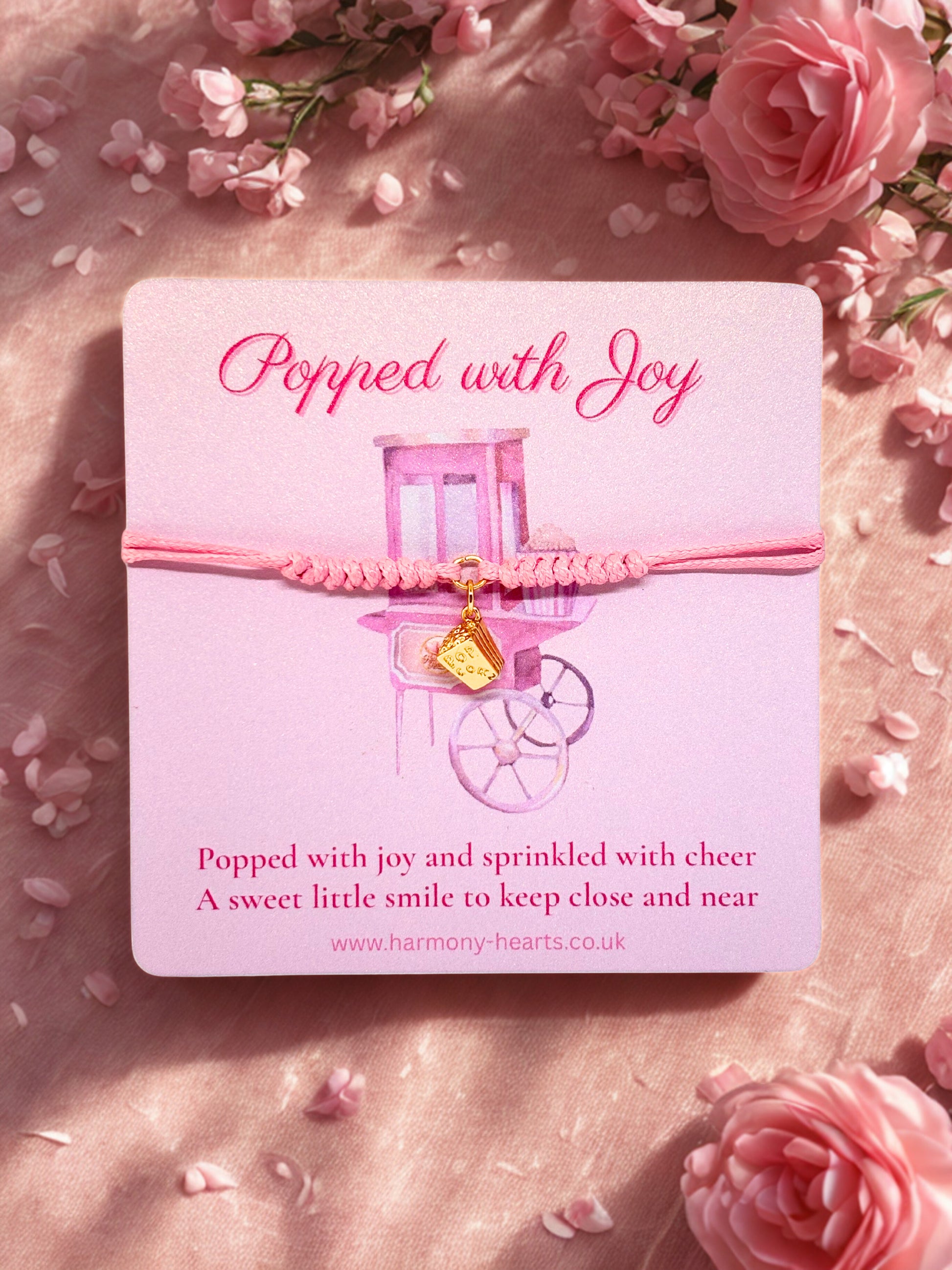 Pink bracelet with a popcorn charm on a matching branded Harmony Hearts card surrounded by pink flowers