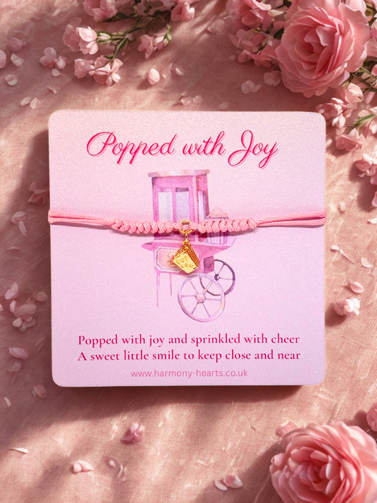 Pink bracelet with a popcorn charm on a matching branded Harmony Hearts card surrounded by pink flowers