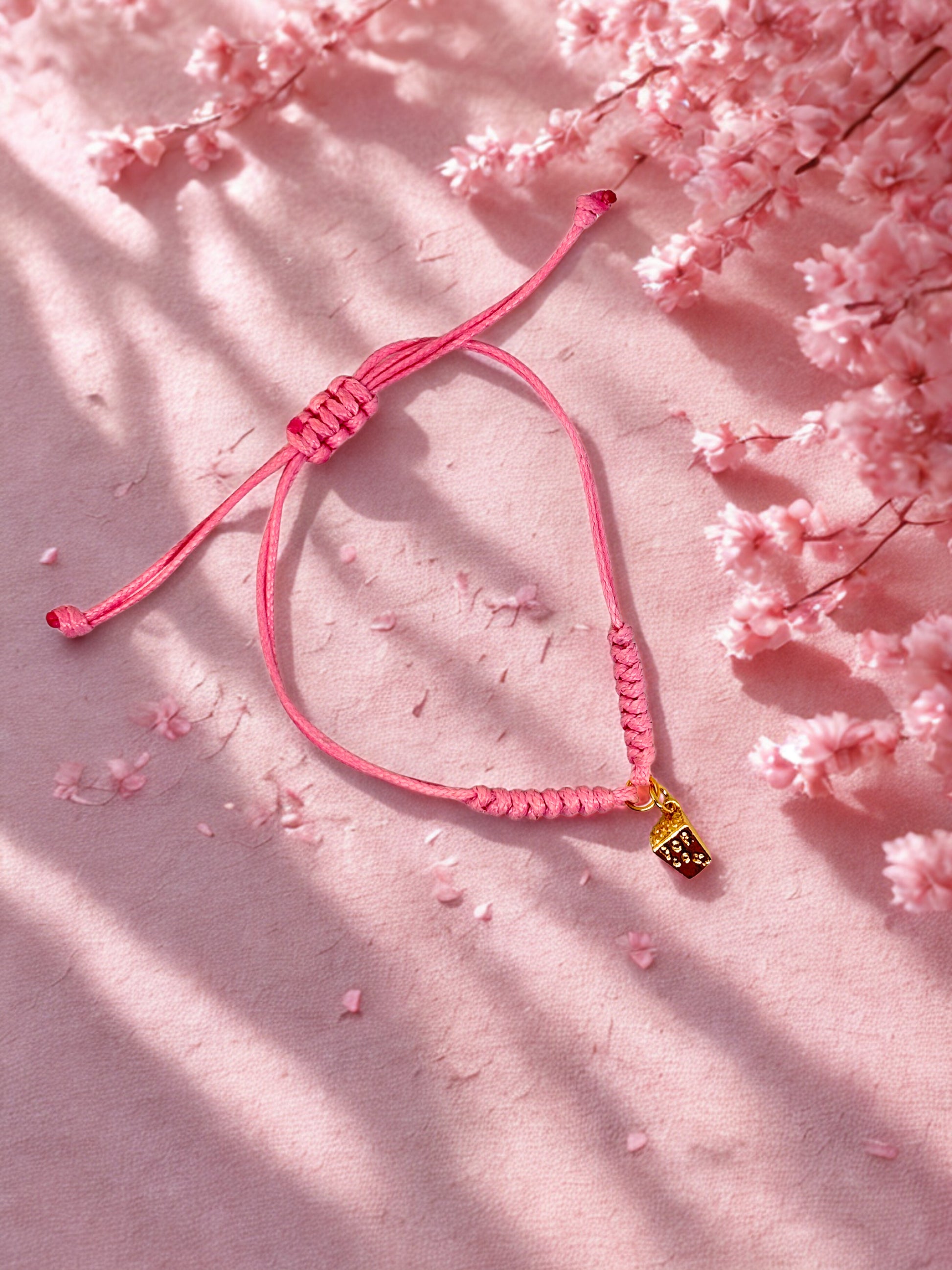 Pink bracelet with a gold popcorn charm on a pink floral background