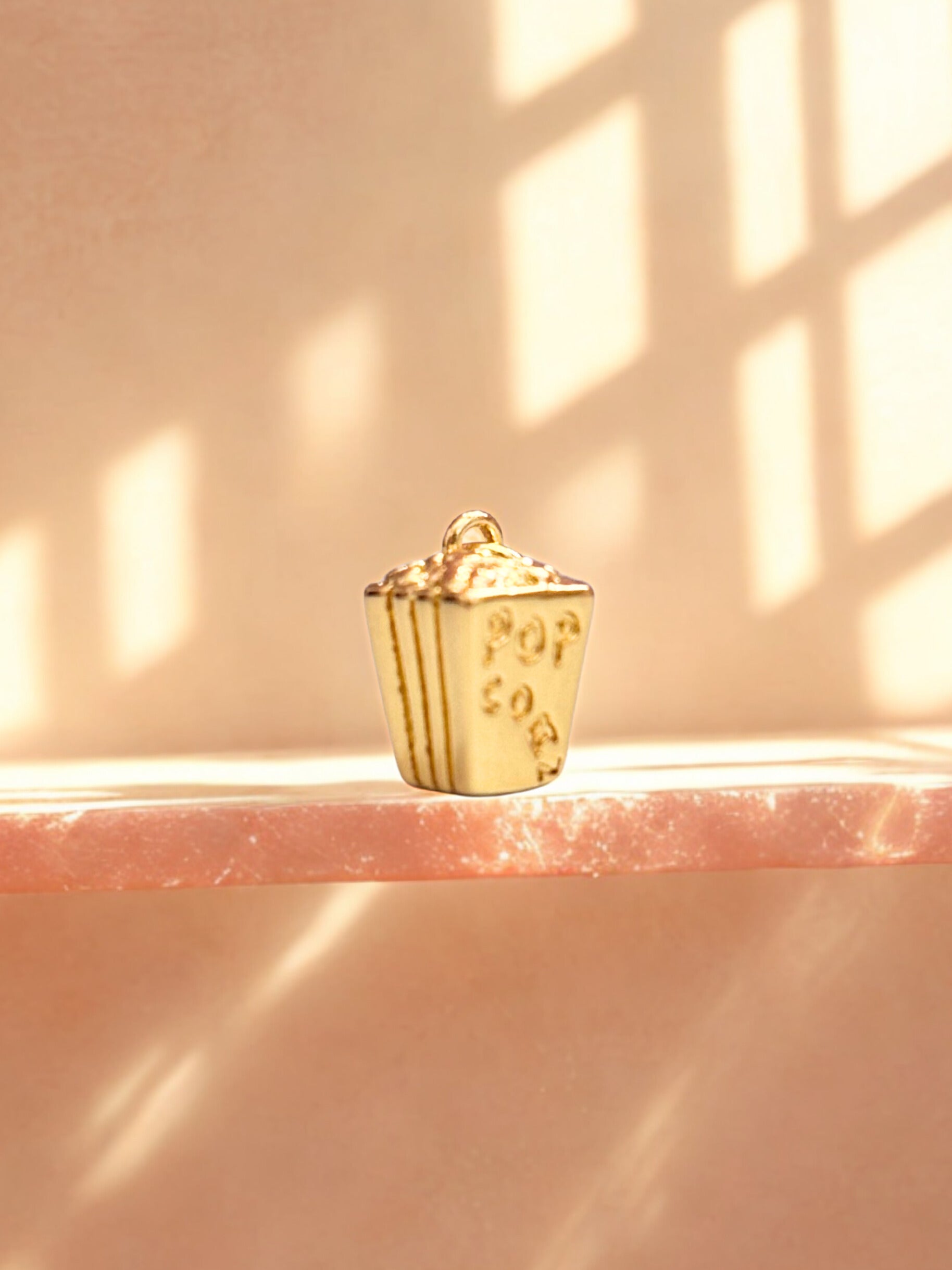 Gold popcorn bucket charm on a pink surface with soft lighting