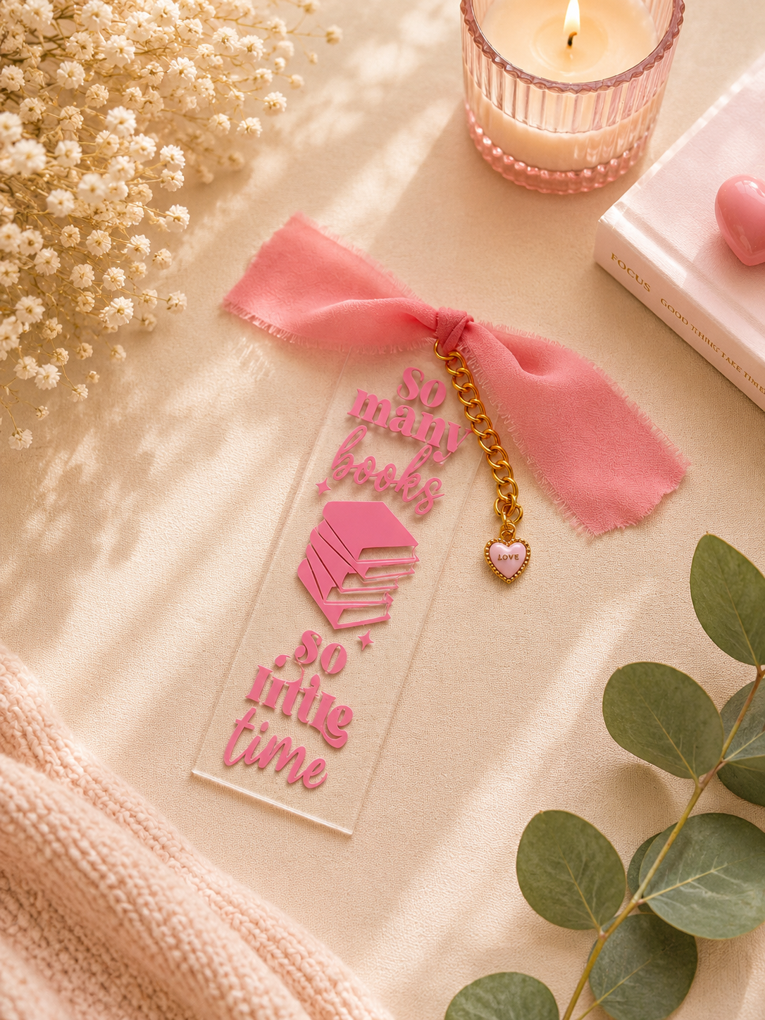 Pink decorative bookmark with a ribbon on a light surface with flowers and a candle.