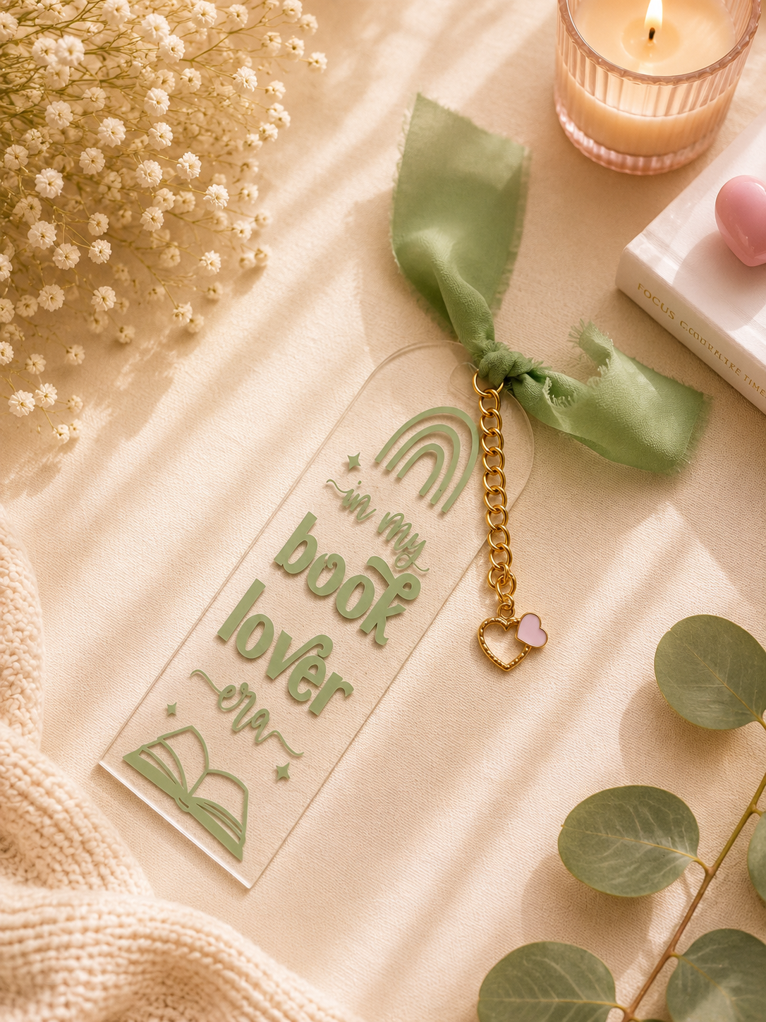 Book lover bookmark with gold chain and pink heart charm on a soft surface with flowers and candle.