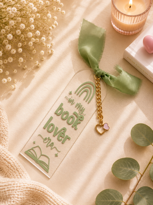 Book lover bookmark with gold chain and pink heart charm on a soft surface with flowers and candle.