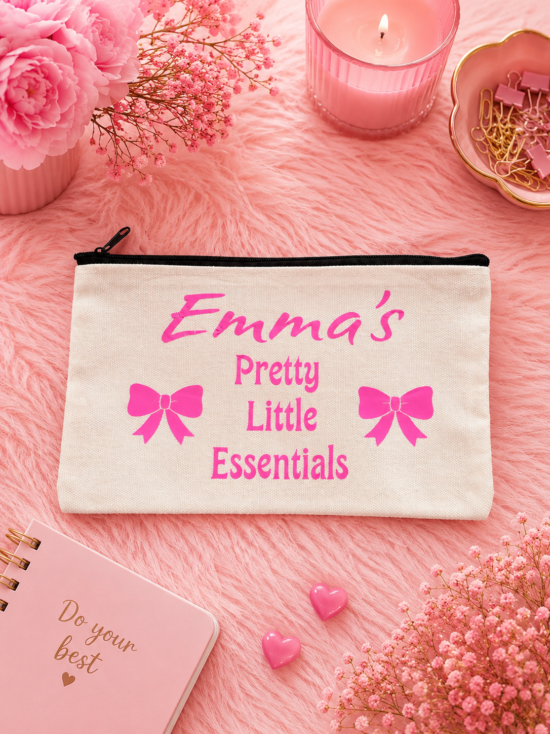 Personalized pouch with 'Emma's Pretty Little Essentials' on a pink surface with flowers and a candle.