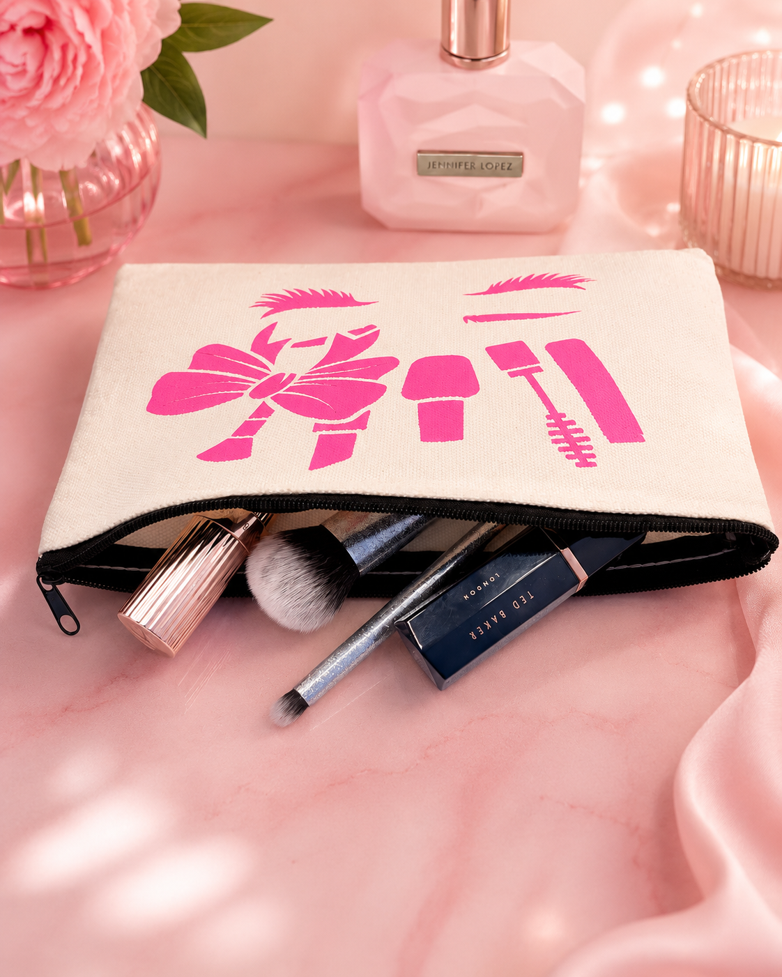 Makeup bag with pink designs on a pink surface with makeup items and flowers.