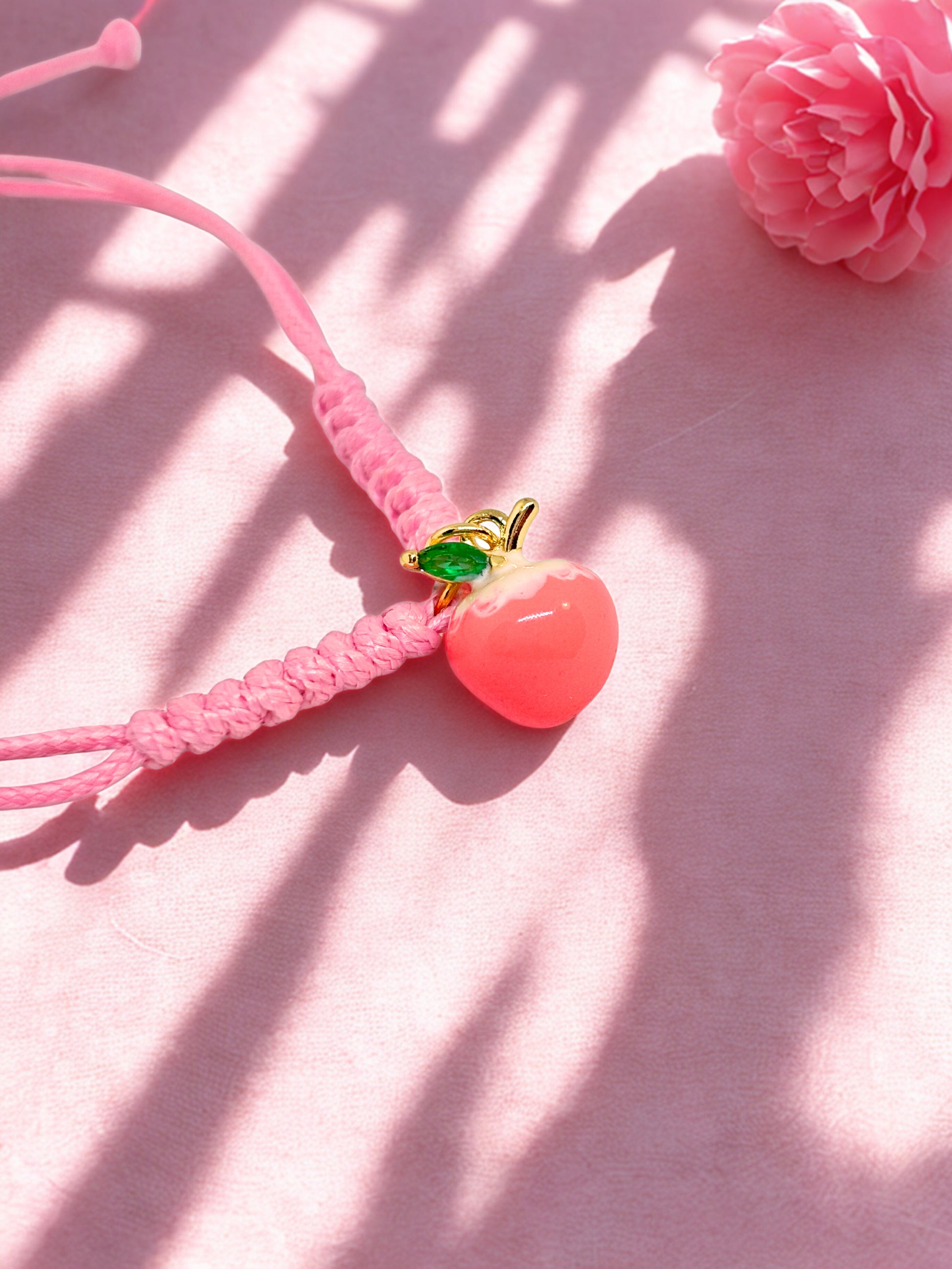 Pink braided bracelet with a peach-shaped charm on a pink background