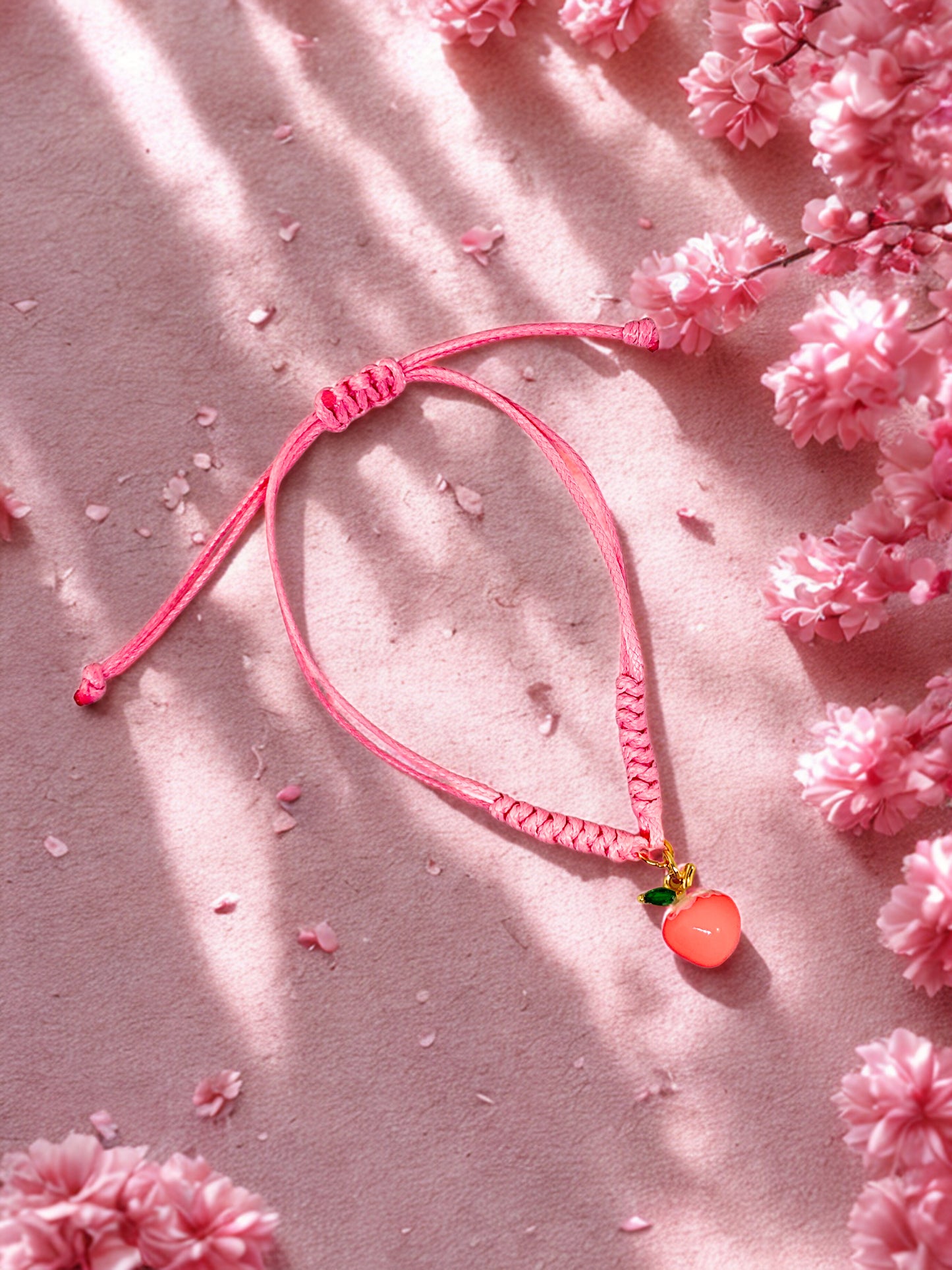 Pink bracelet with a peach charm on a pink surface with cherry blossoms