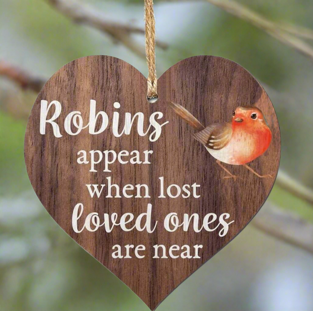 Wooden heart-shaped ornament with a robin illustration and text on a blurred natural background