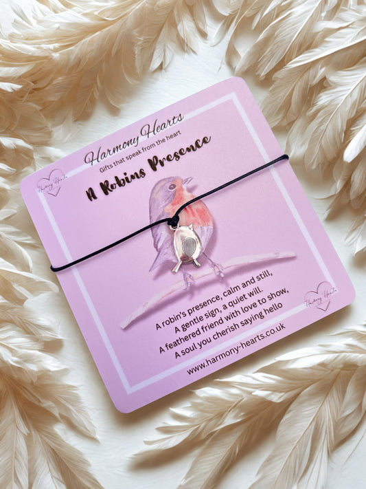 Bracelet with a robin design on a pink card with text, placed on a fluffy white surface.