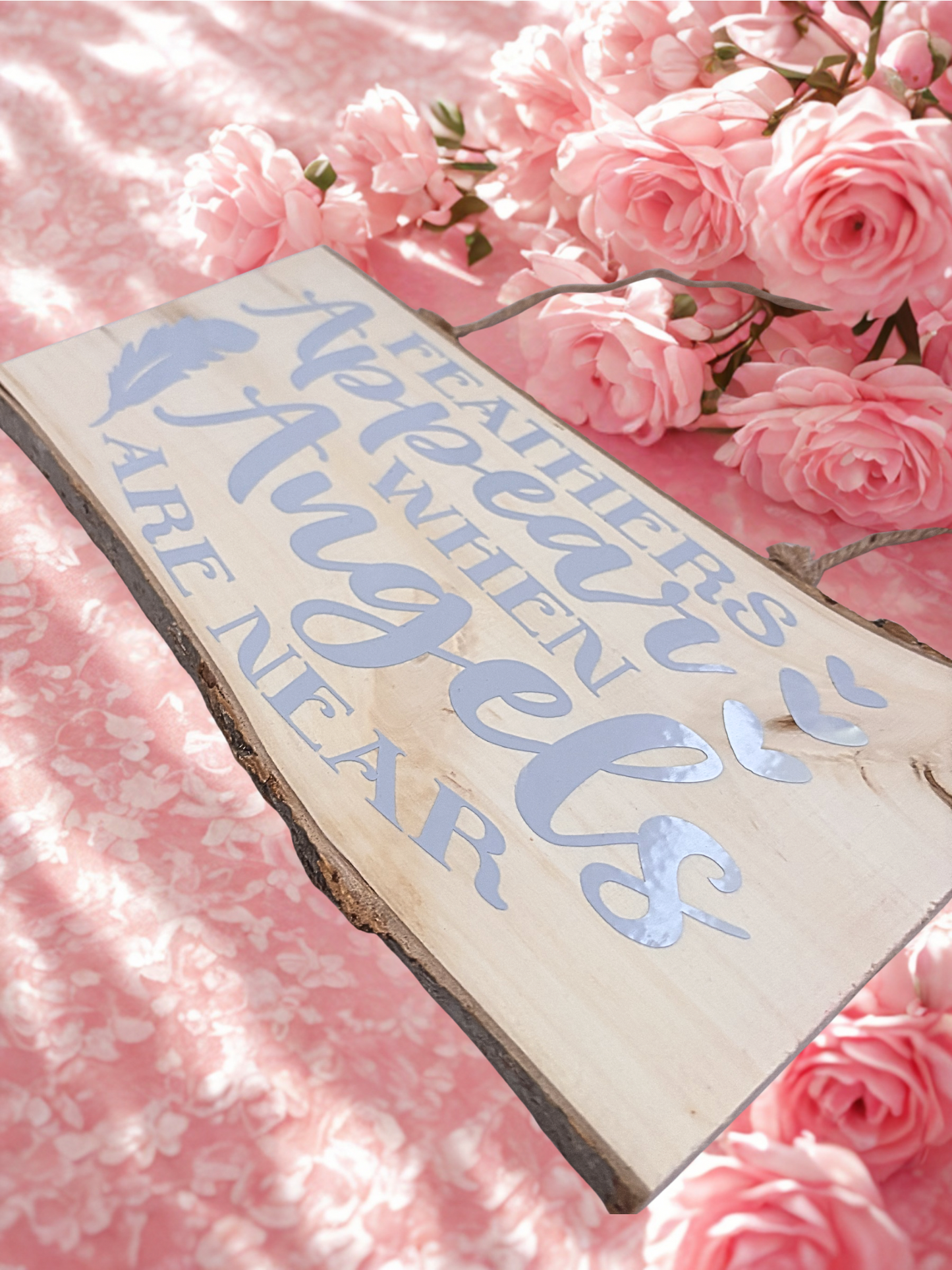 Wooden sign with 'Feathers Appear When Angels are Near' text on a pink floral background