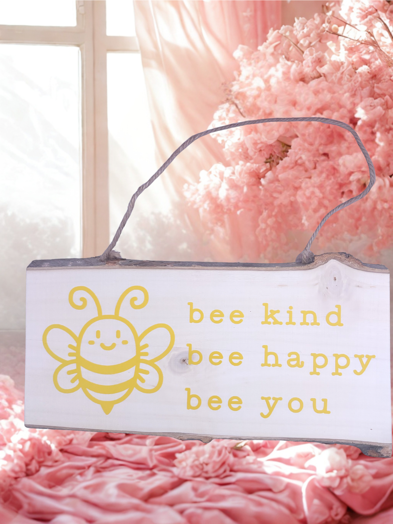 Decorative sign with a bee illustration and text 'bee kind bee happy bee you' on a pink floral background.