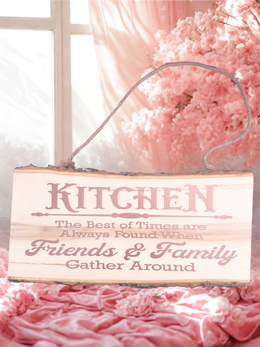 Decorative wooden sign with text 'Kitchen: The best of times are always found when friends & family gather around' on a pink floral background.