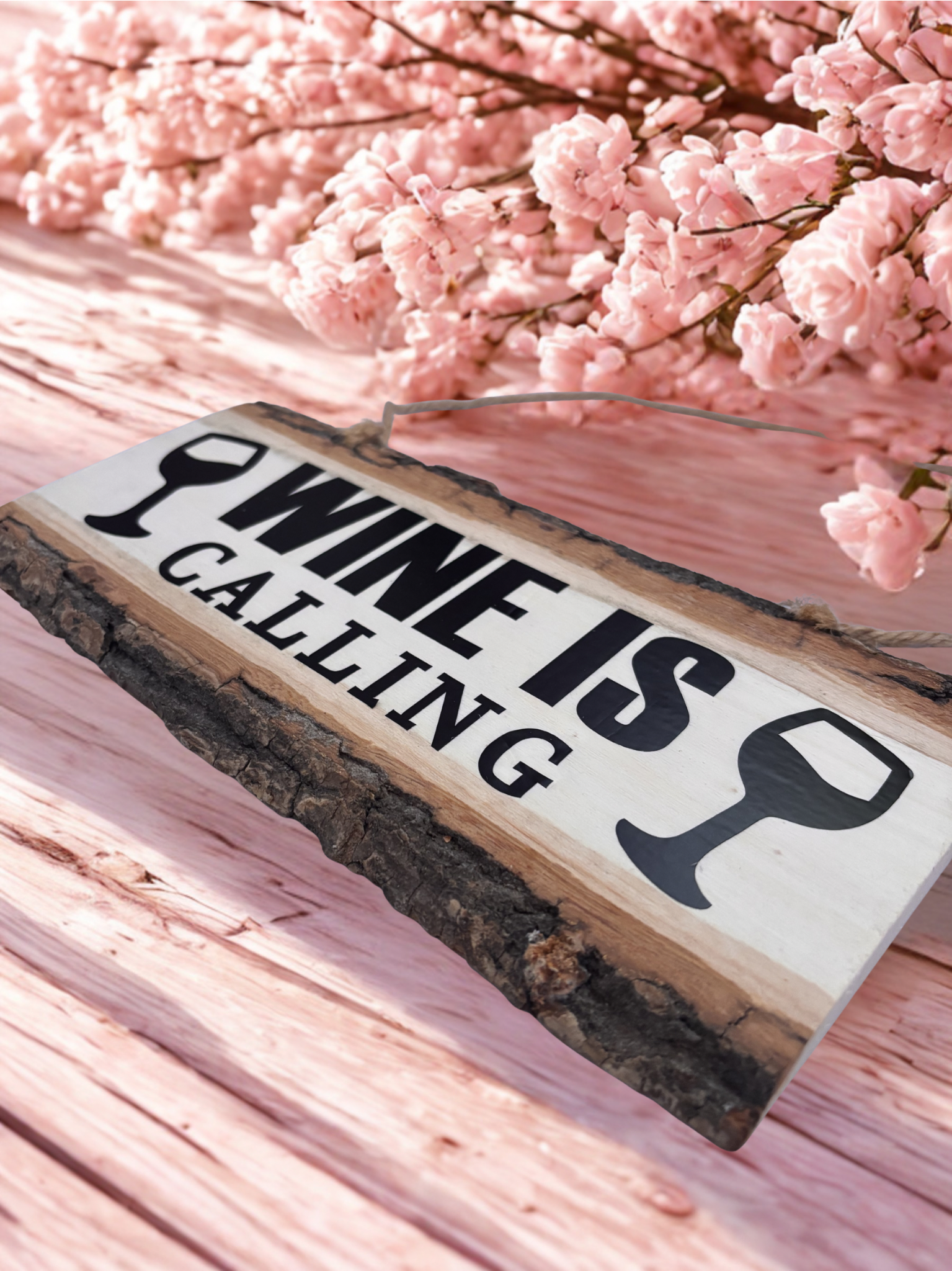 Wooden sign with 'Wine is Calling' text against a pink cherry blossom background