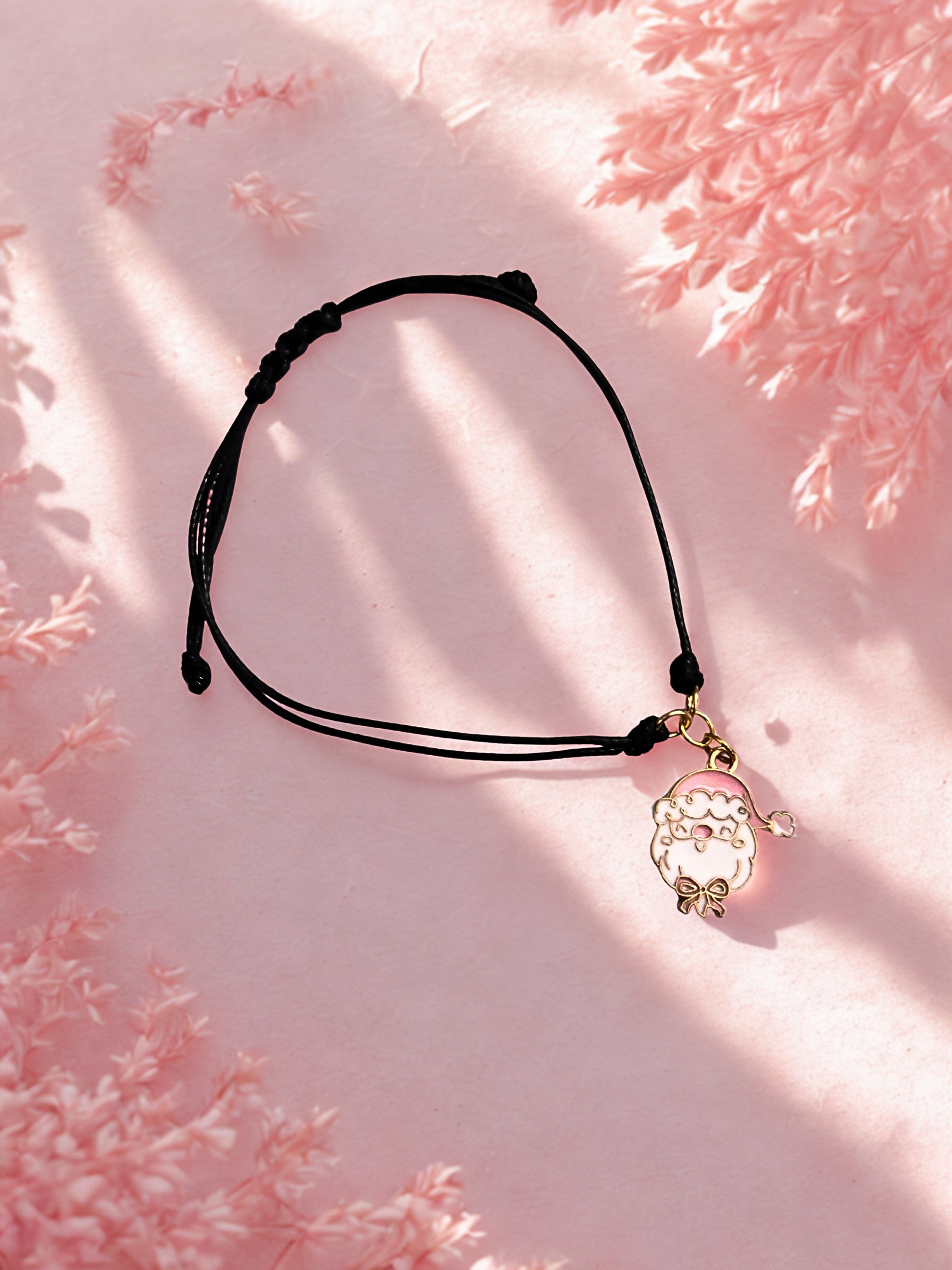Black cord vharm bracelet with a decorative Santa charm on a pink floral background