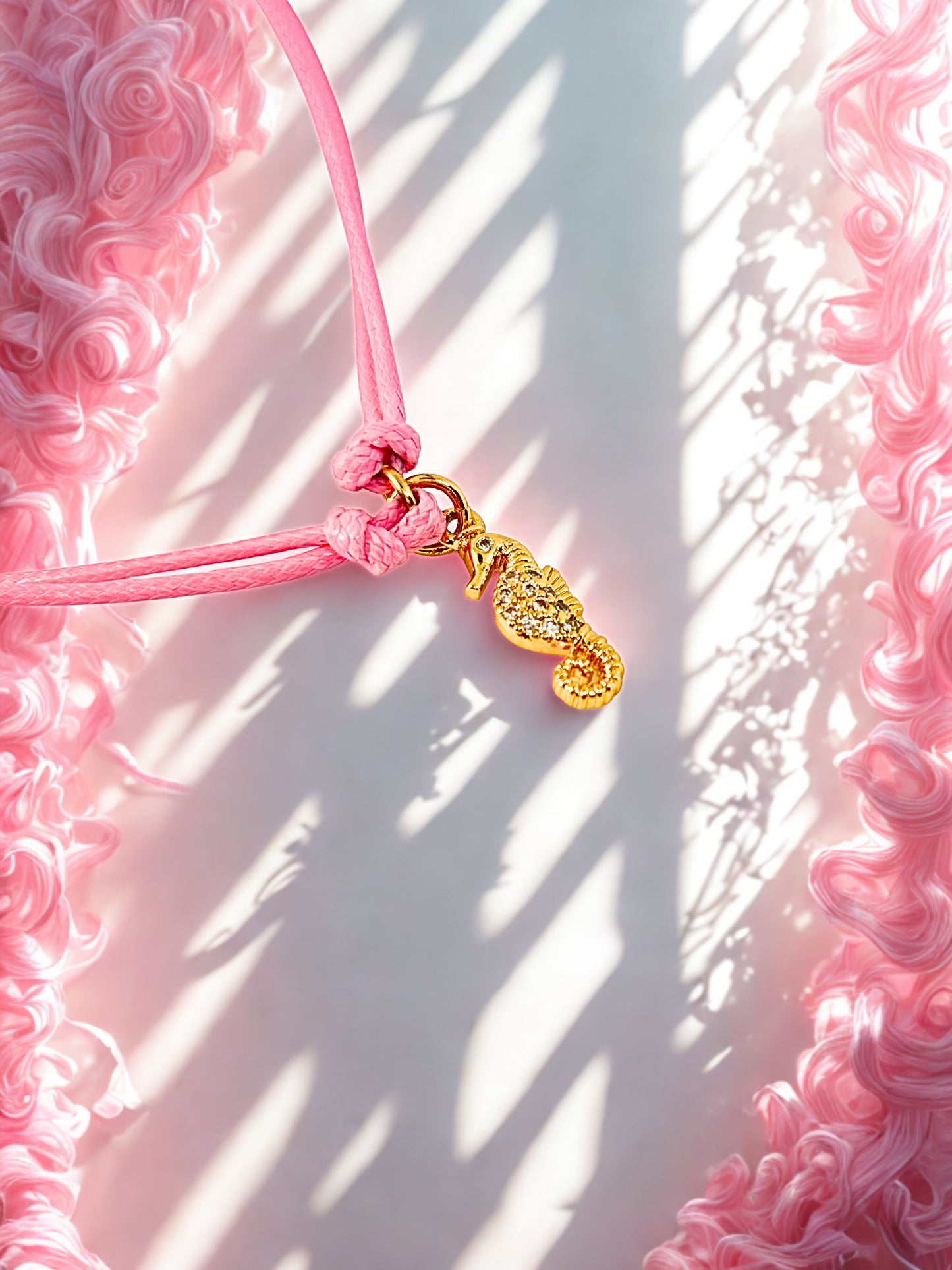 Pink cord with a gold seahorse charm on a pink textured background