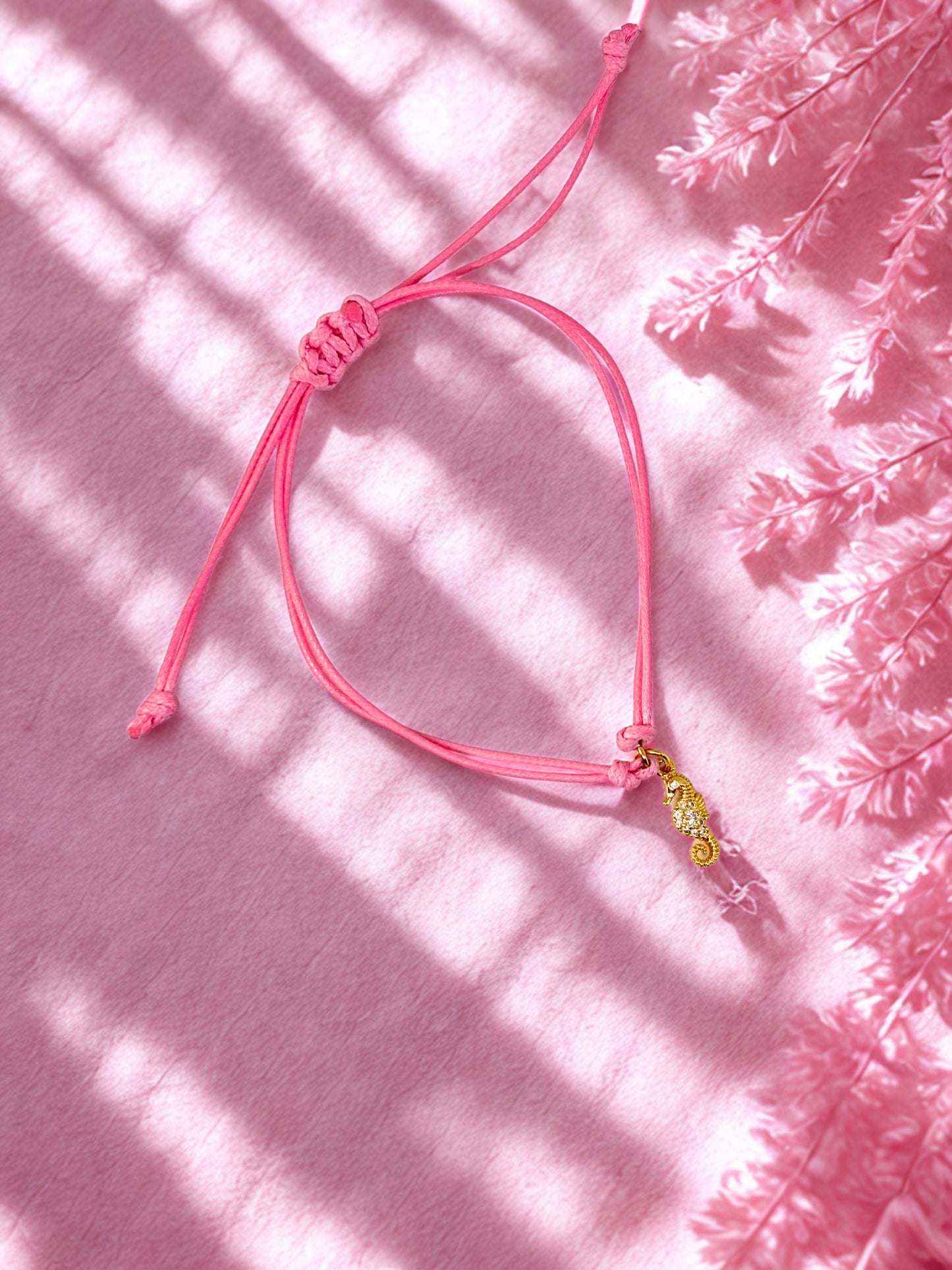 Pink bracelet with gold seahorse charm on a pink textured background