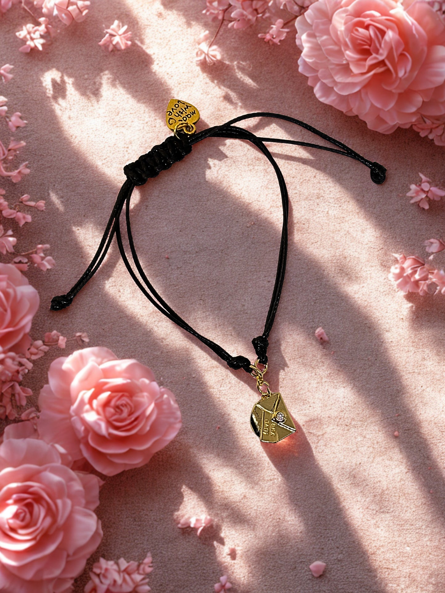 Black cord bracelet with gold envelope charm on a pink floral background