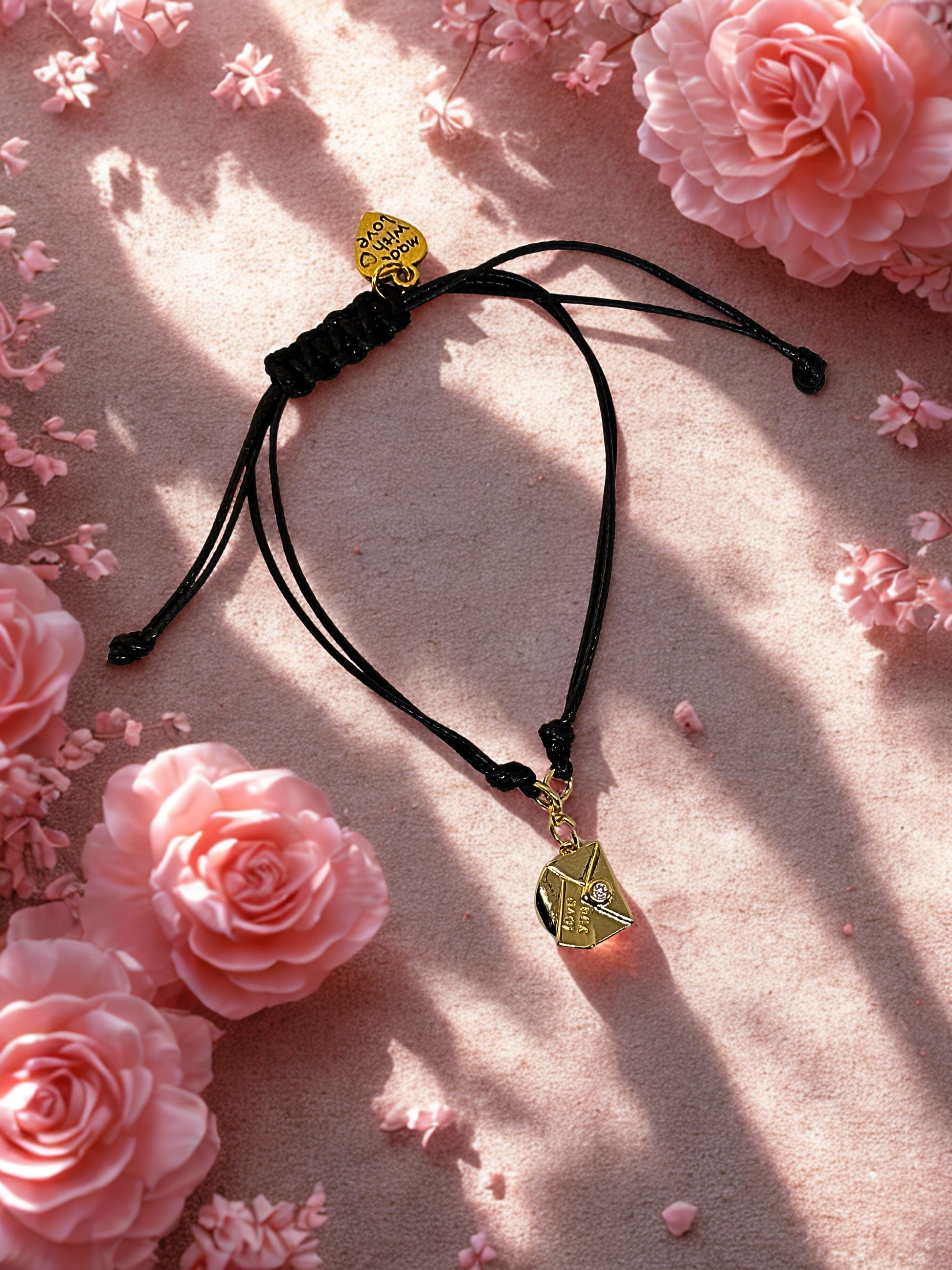 Black cord bracelet with gold envelope charm on a pink floral background