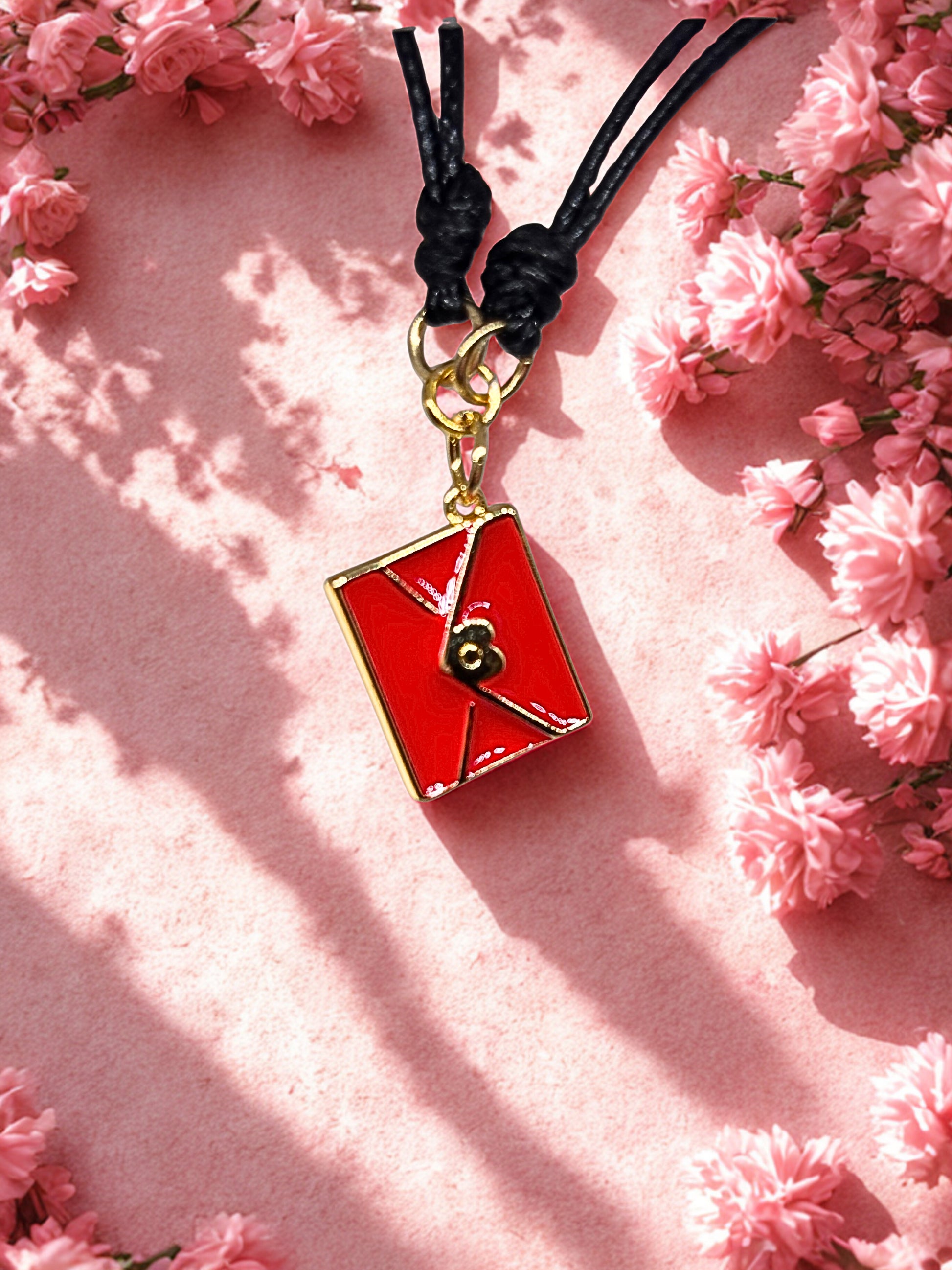 Red envelope charm bracelet on a black cord with pink flowers in the background