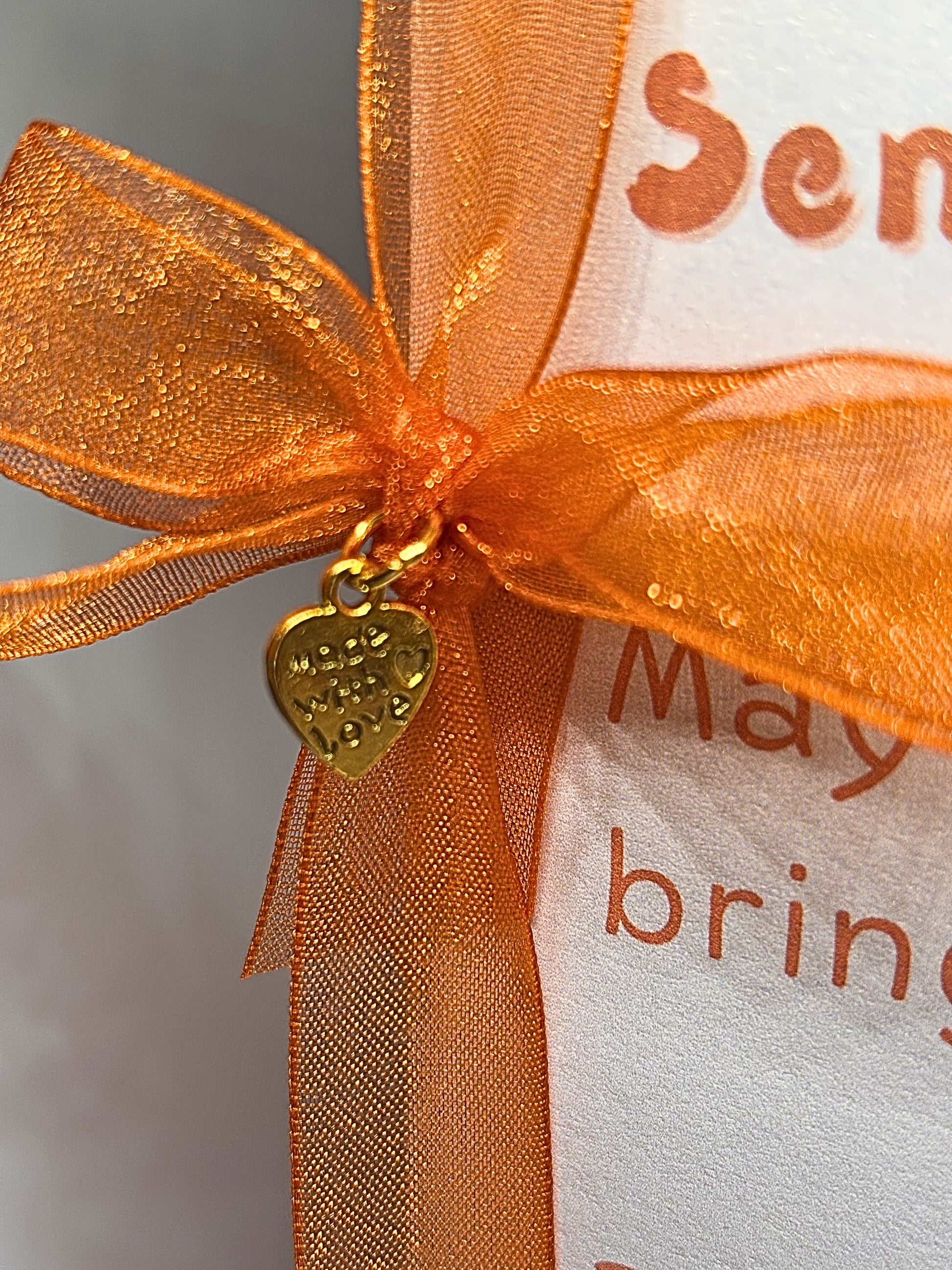 Orange ribbon with a gold heart charm on a white card with text.