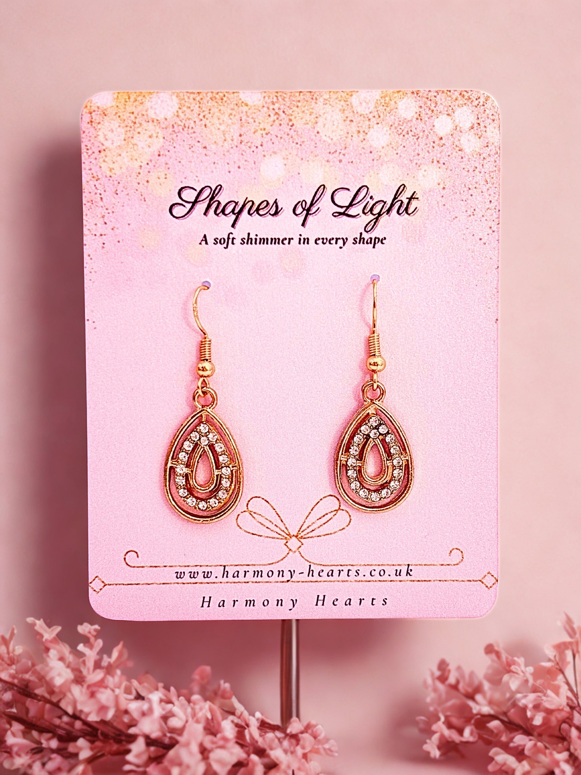 Teardrop-shaped earrings on a 'Shapes of Light' branded card with a soft pink background.