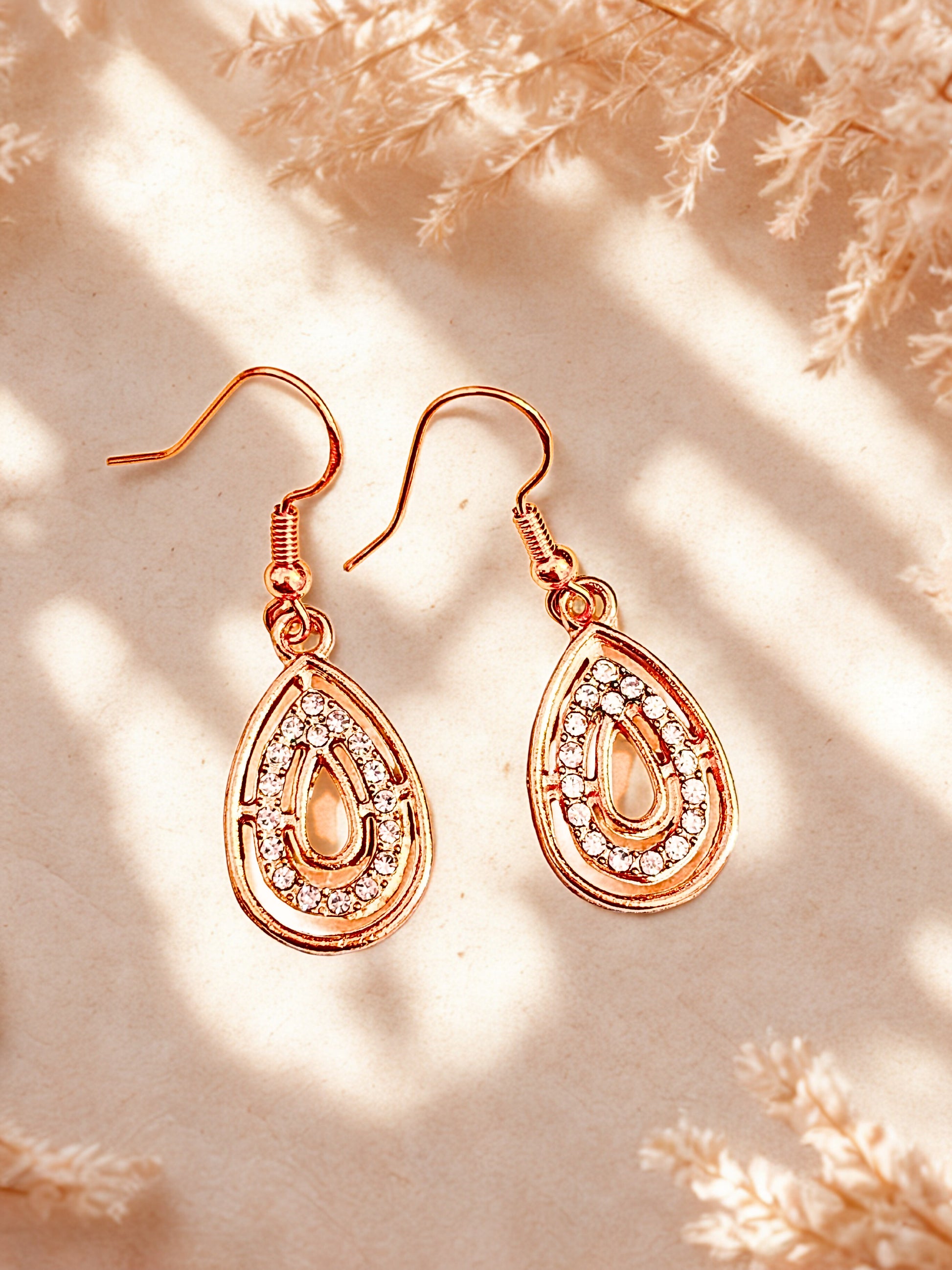 Rose gold teardrop earrings with clear stones on a beige background