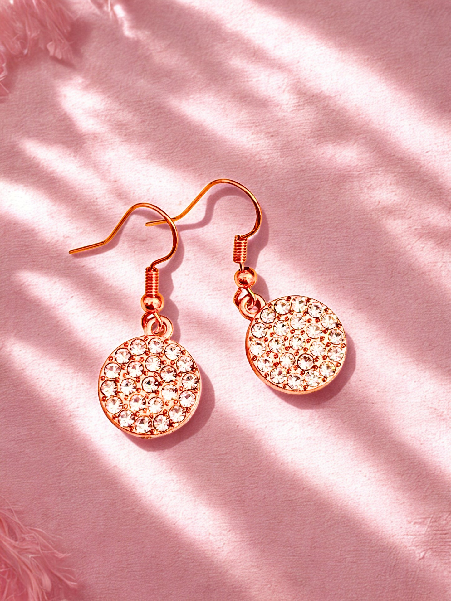 Gold round sparkly earrings against a pink background