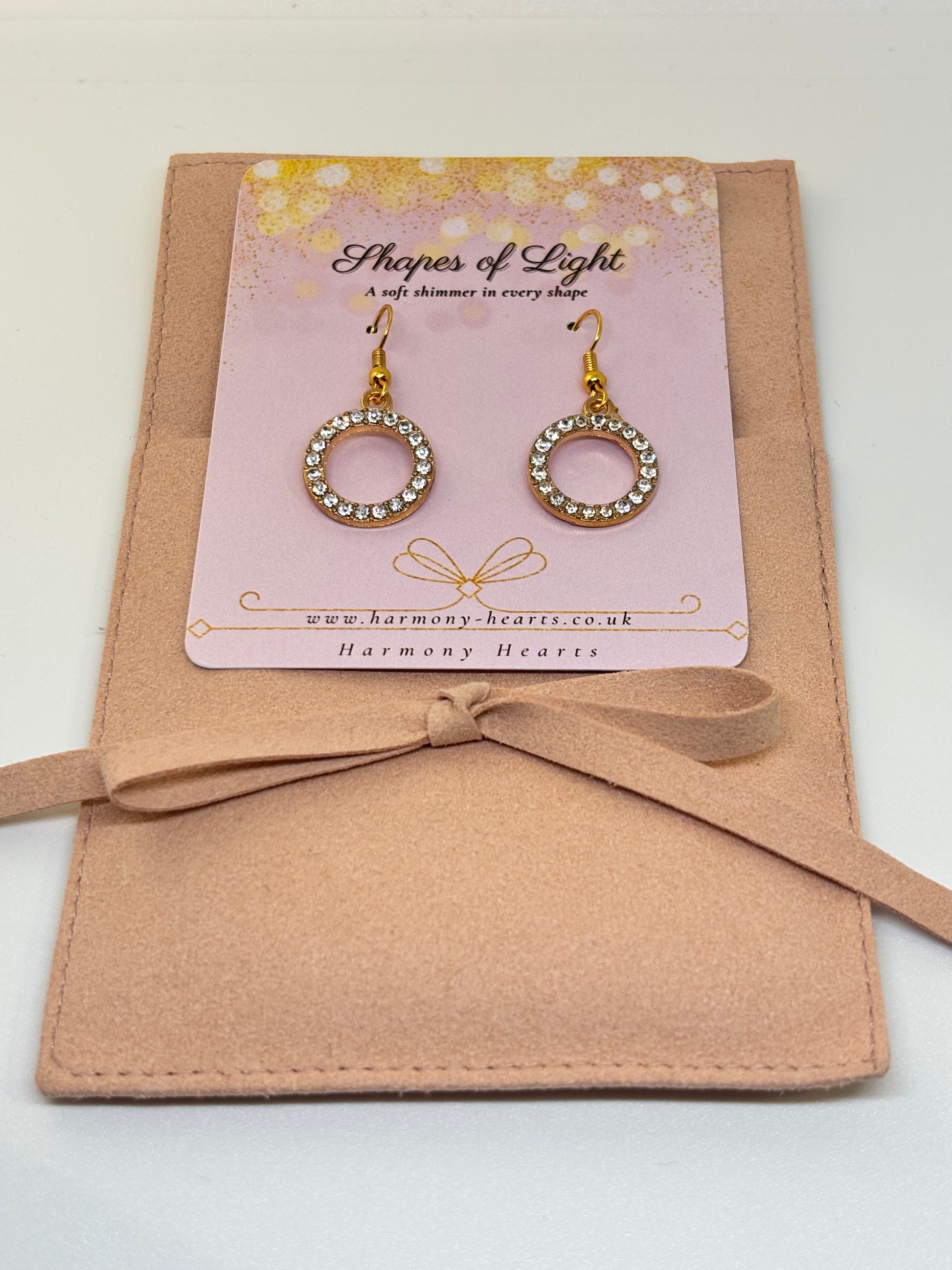 Gold hoop earrings with crystals on a 'Shapes of Light' card, placed on a beige fabric surface.