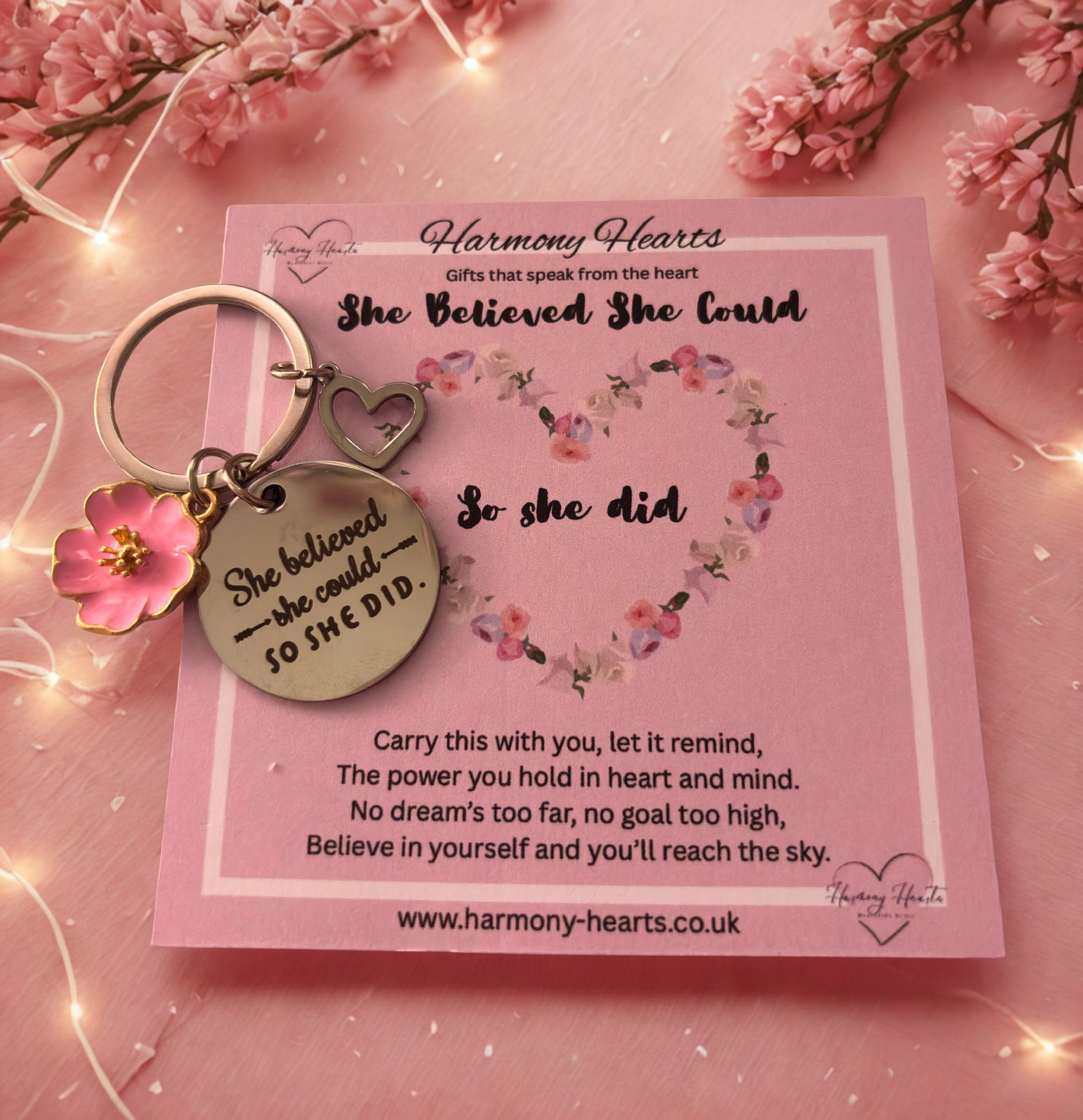 Keychain with motivational quote on a pink card with floral design, surrounded by pink flowers and lights.