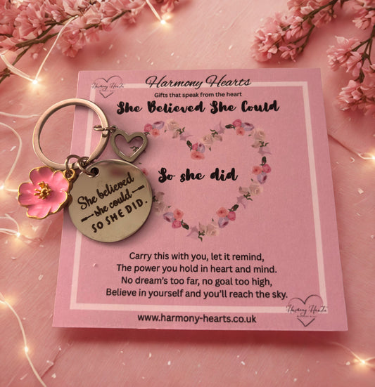 Keychain with motivational quote on a pink card with floral design, surrounded by pink flowers and lights.