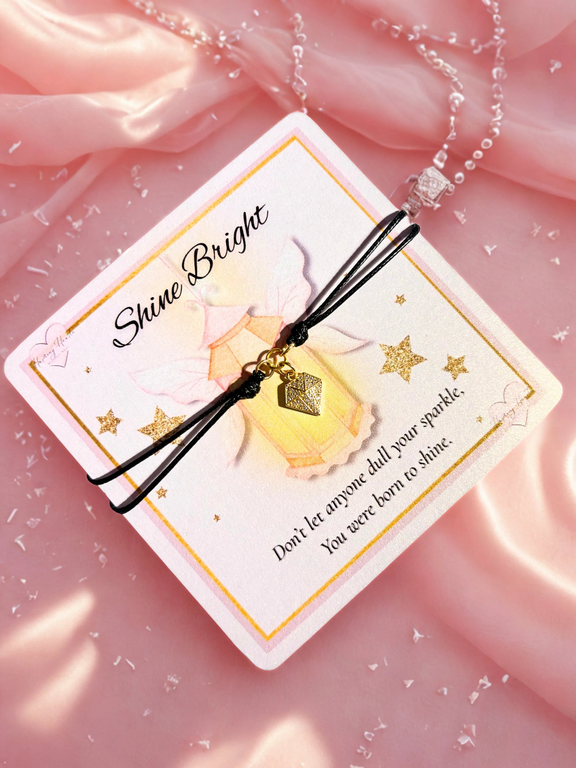 Bracelet with diamond shaped charm on a 'Shine Bright' card against a pink background