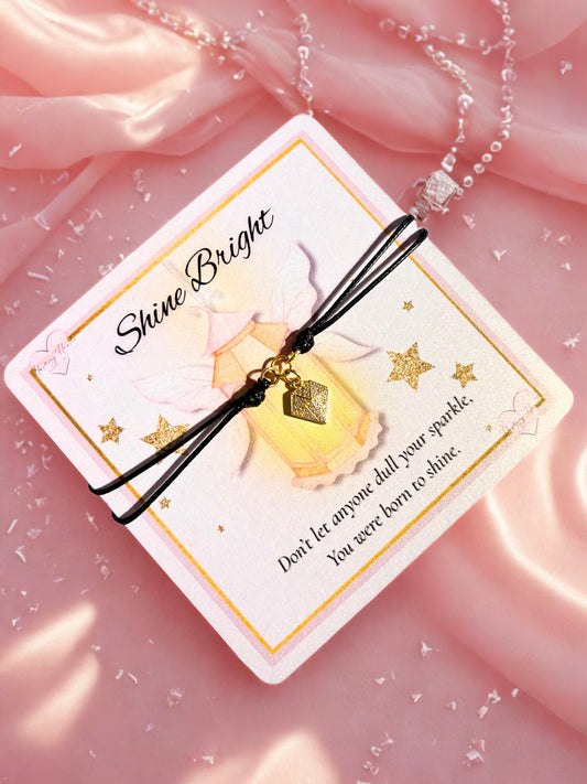 Bracelet with diamond shaped charm on a 'Shine Bright' card against a pink background