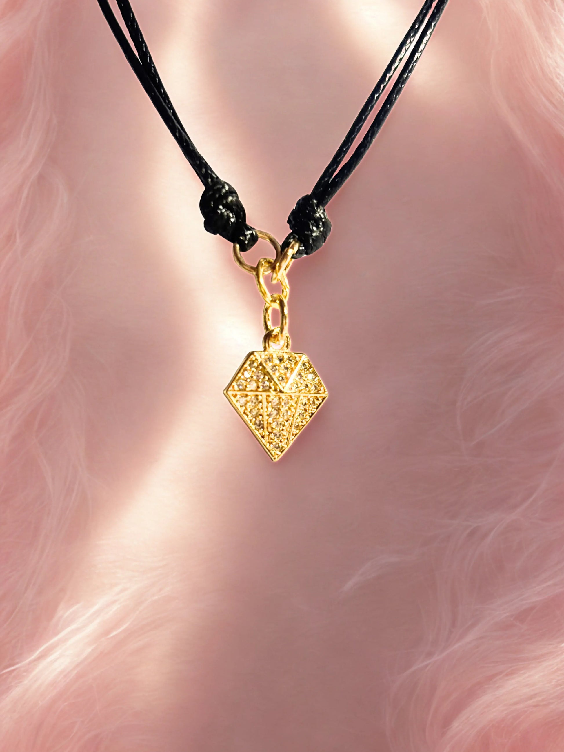 Gold diamond shape charm on a black cord against a pink fur background