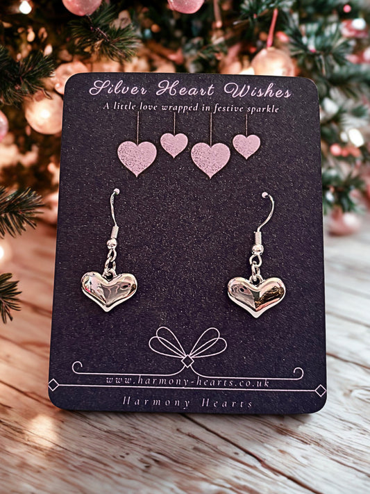 Heart-shaped earrings on a 'Silver Heart Wishes' card with Christmas tree in the background