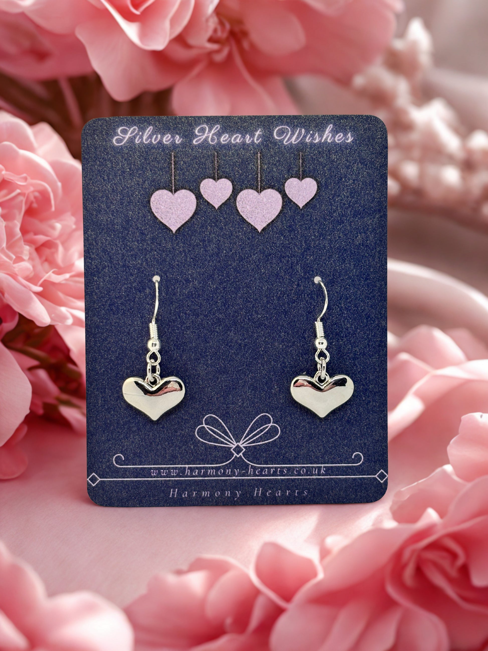 Heart-shaped earrings on a 'Silver Heart Wishes' card with pink flowers in the background