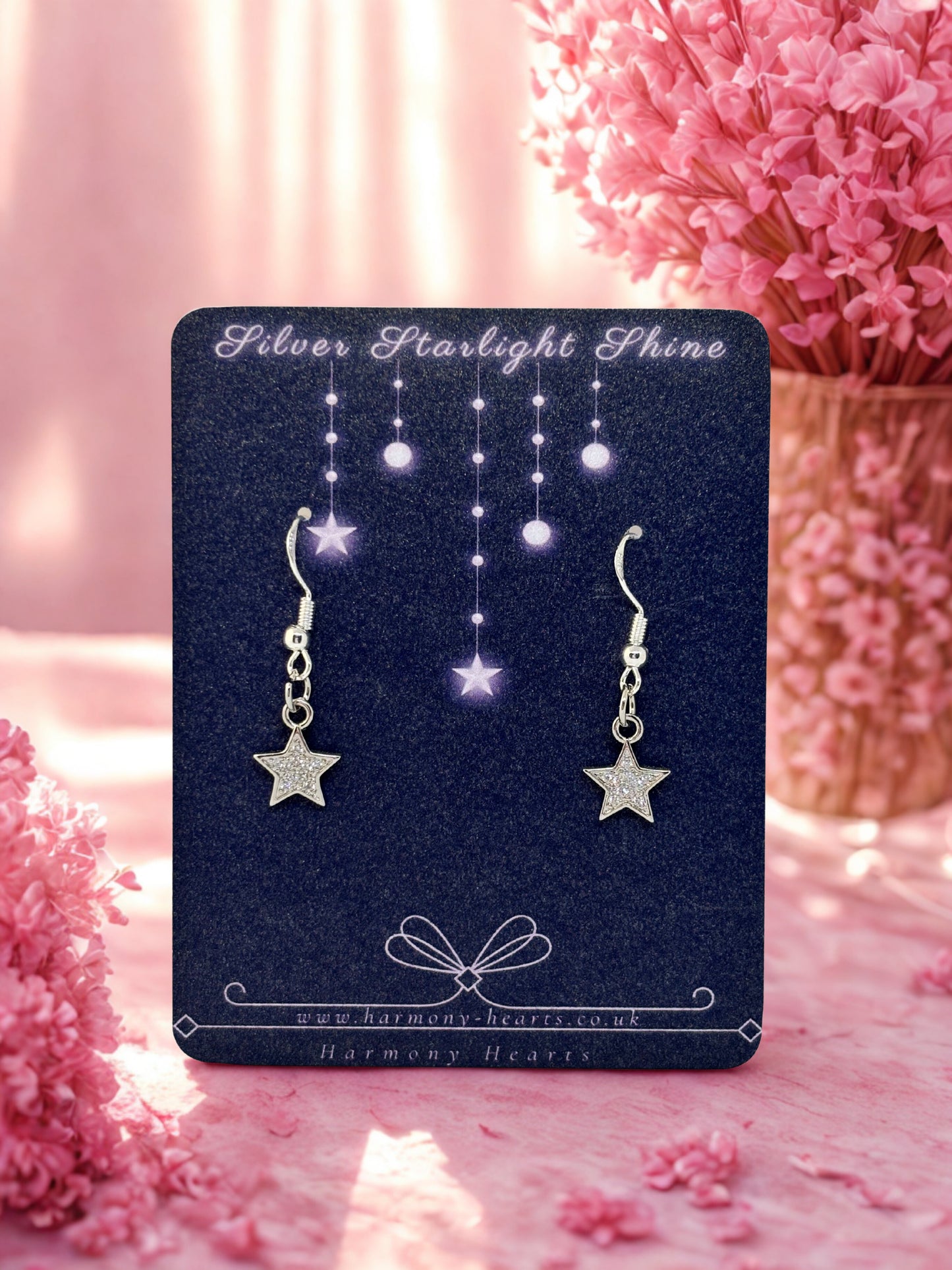 Star-shaped earrings on a branded card with pink flowers in the background