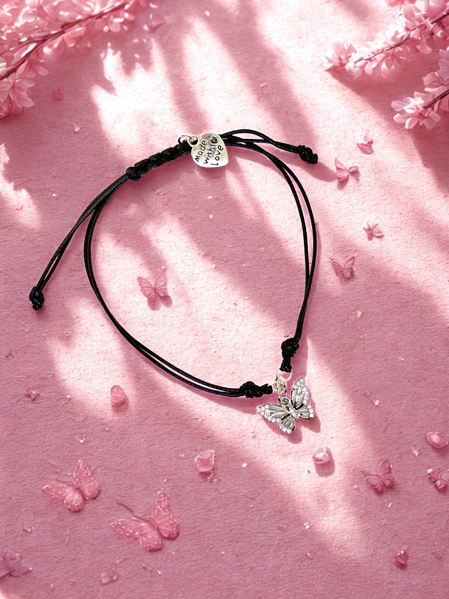 Black bracelet with silver butterfly charm on a pink surface with butterfly decorations
