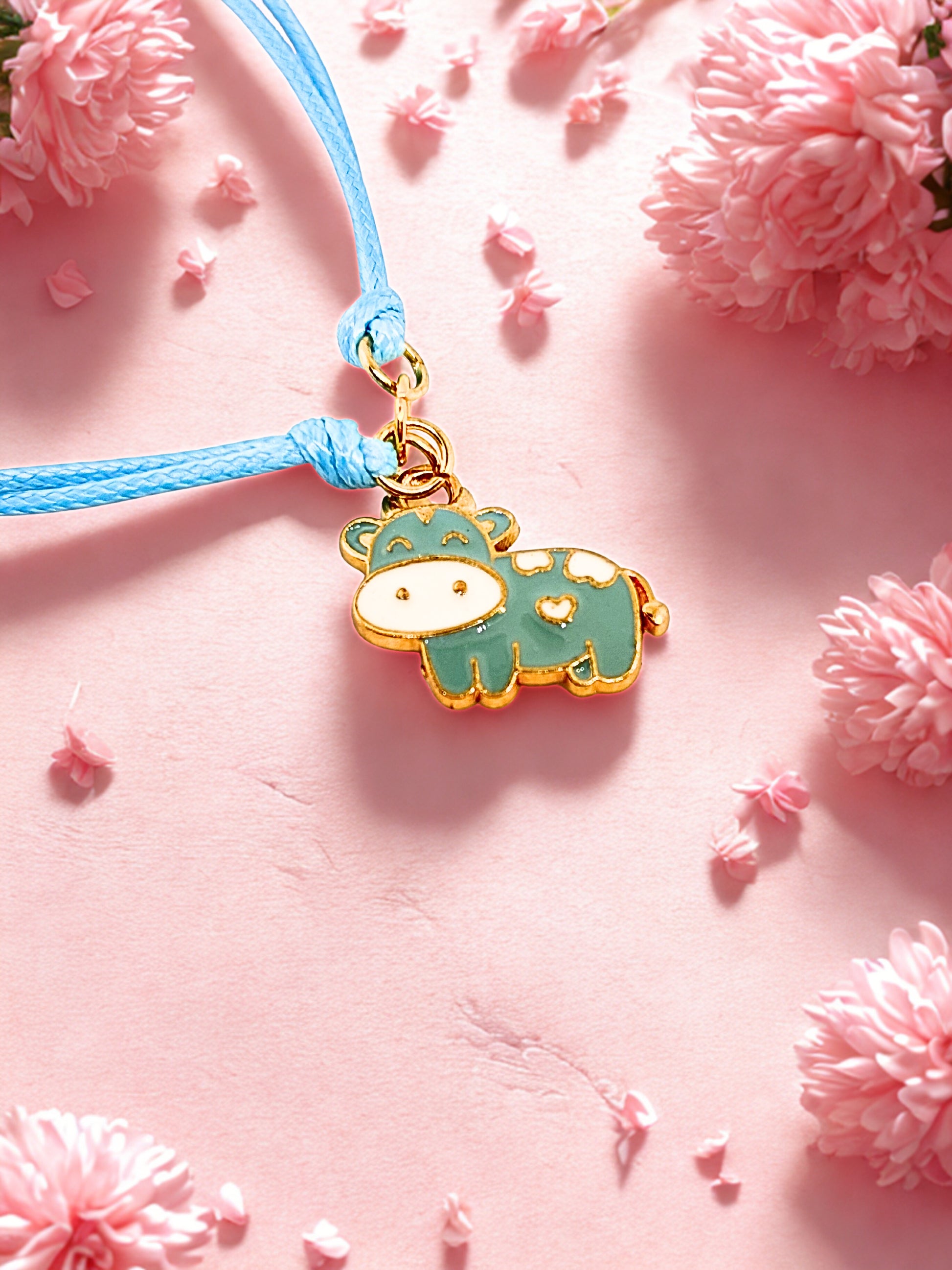 Blue and gold cow charm on a blue cord bracelet against a pink floral background