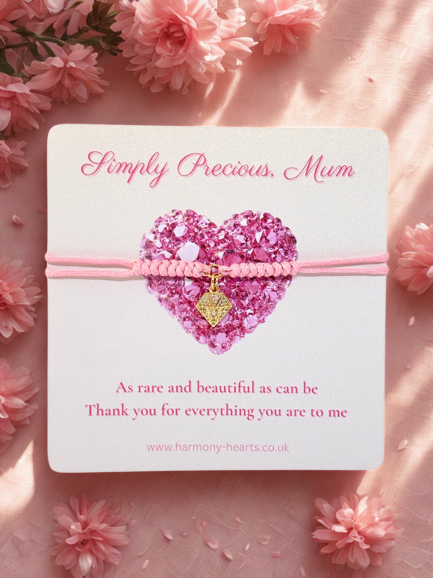 Pink bracelet with a gold diamond shaped charm on a card surrounded by pink flowers.