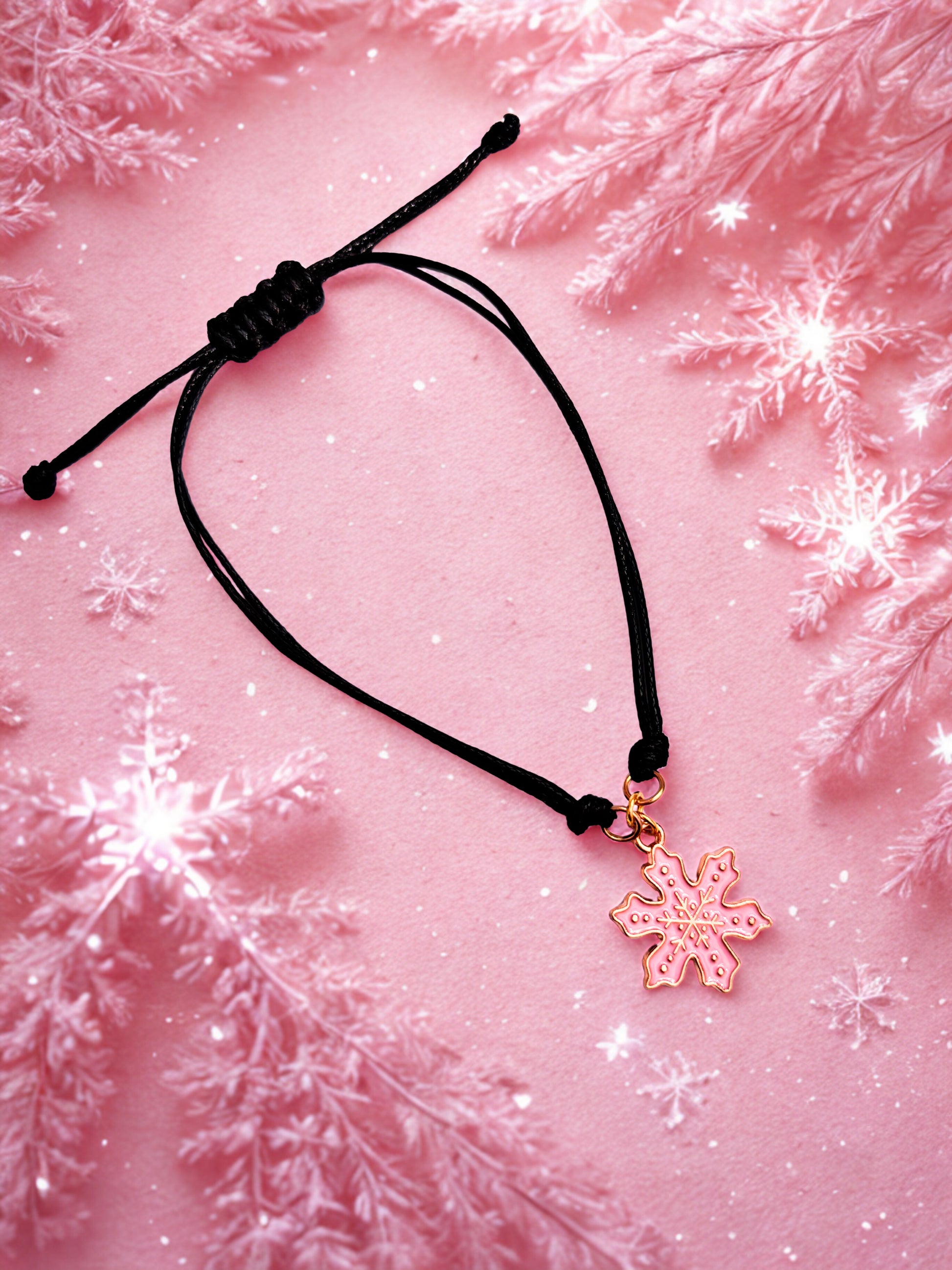 Black cord bracelet with a pink snowflake charm on a pink background with snowflake decorations