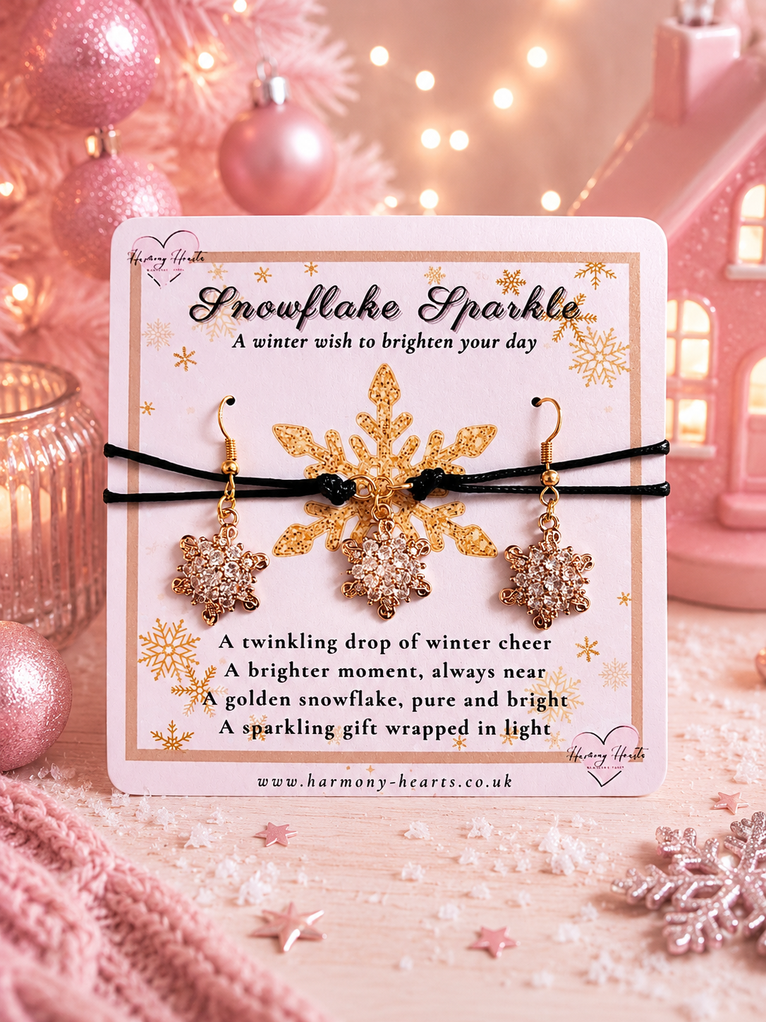 A pair of gold and crystal snowflake drop earrings and matching cord bracelet displayed on a white gift card labeled 'Snowflake Sparkle' with a poem, set against a pink holiday-themed background with ornaments and lights.
