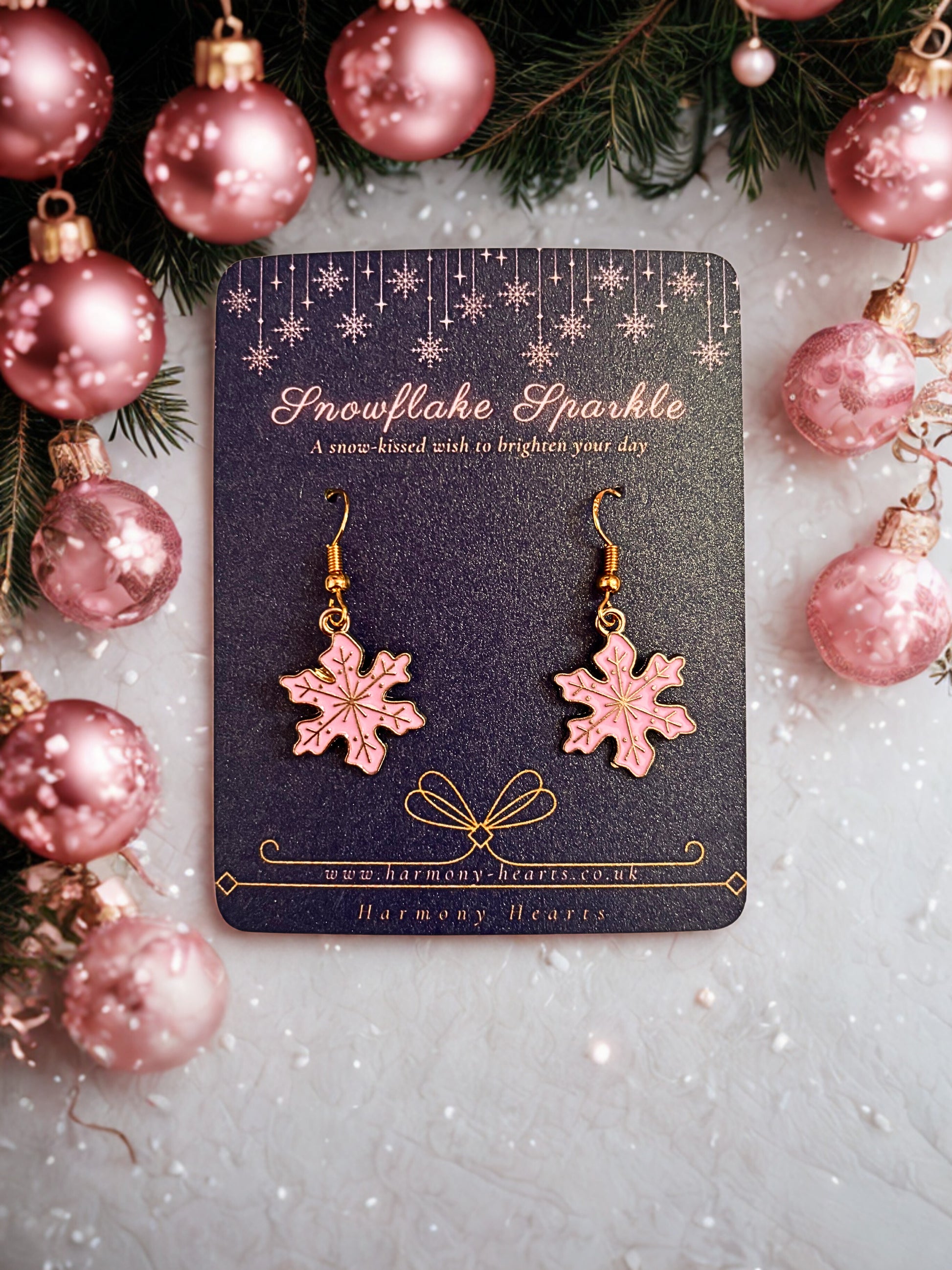 Pink snowflake earrings on a 'Snowflake Sparkle' card with Christmas decorations.