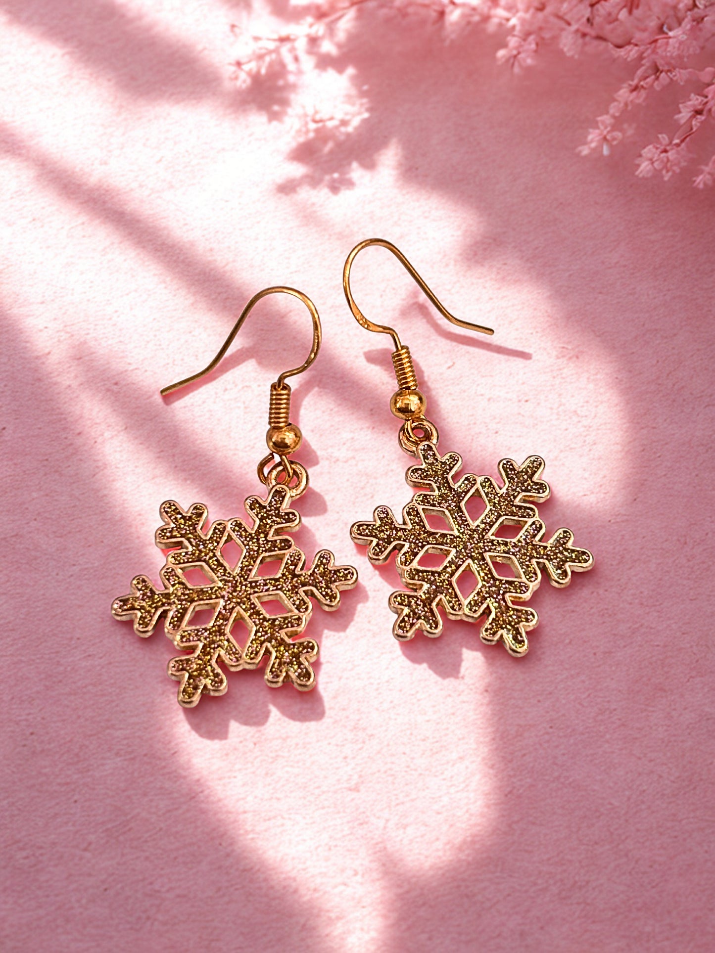 Gold snowflake earrings on a pink background