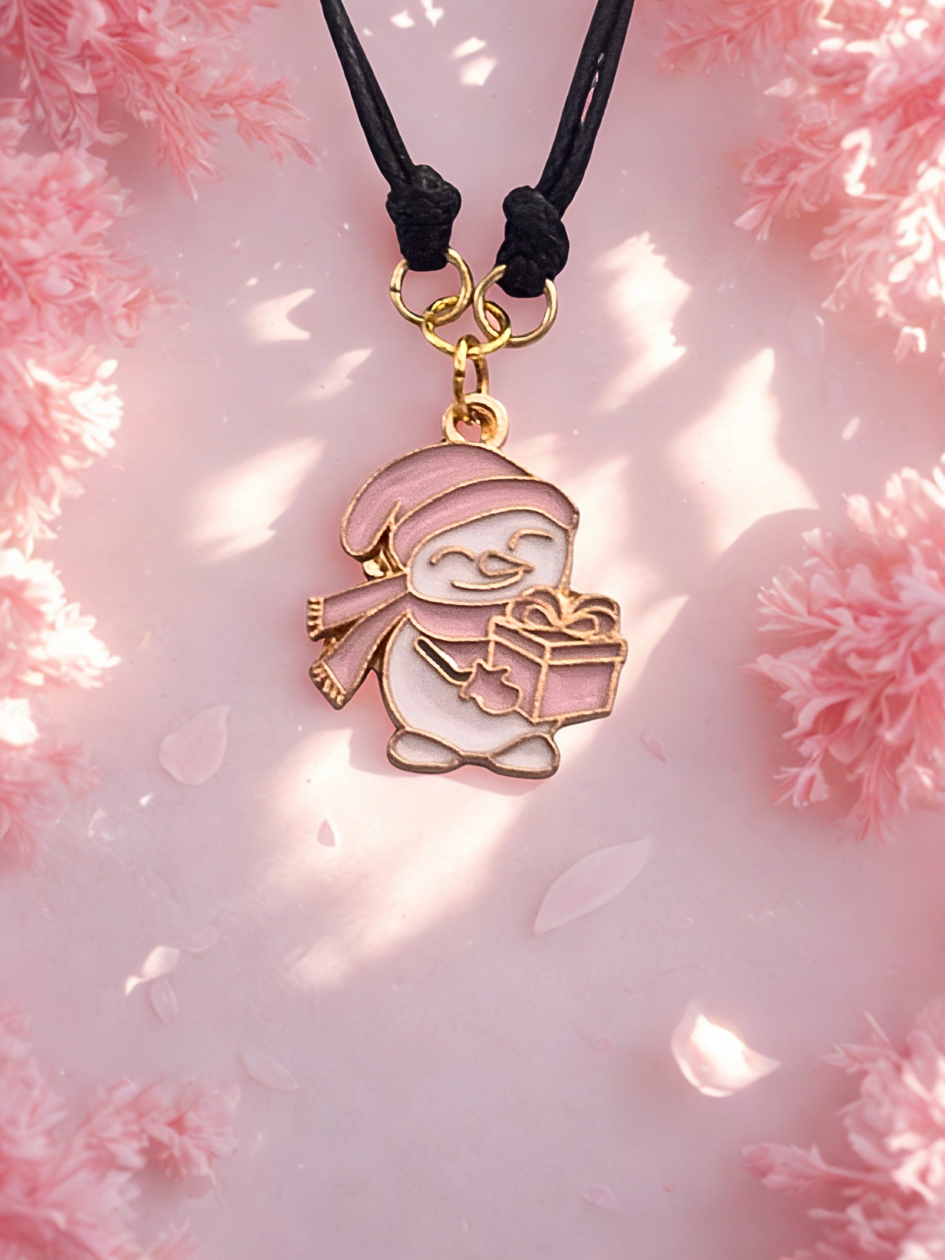 Snowman charm bracelet with a gift on a black cord against a pink floral background