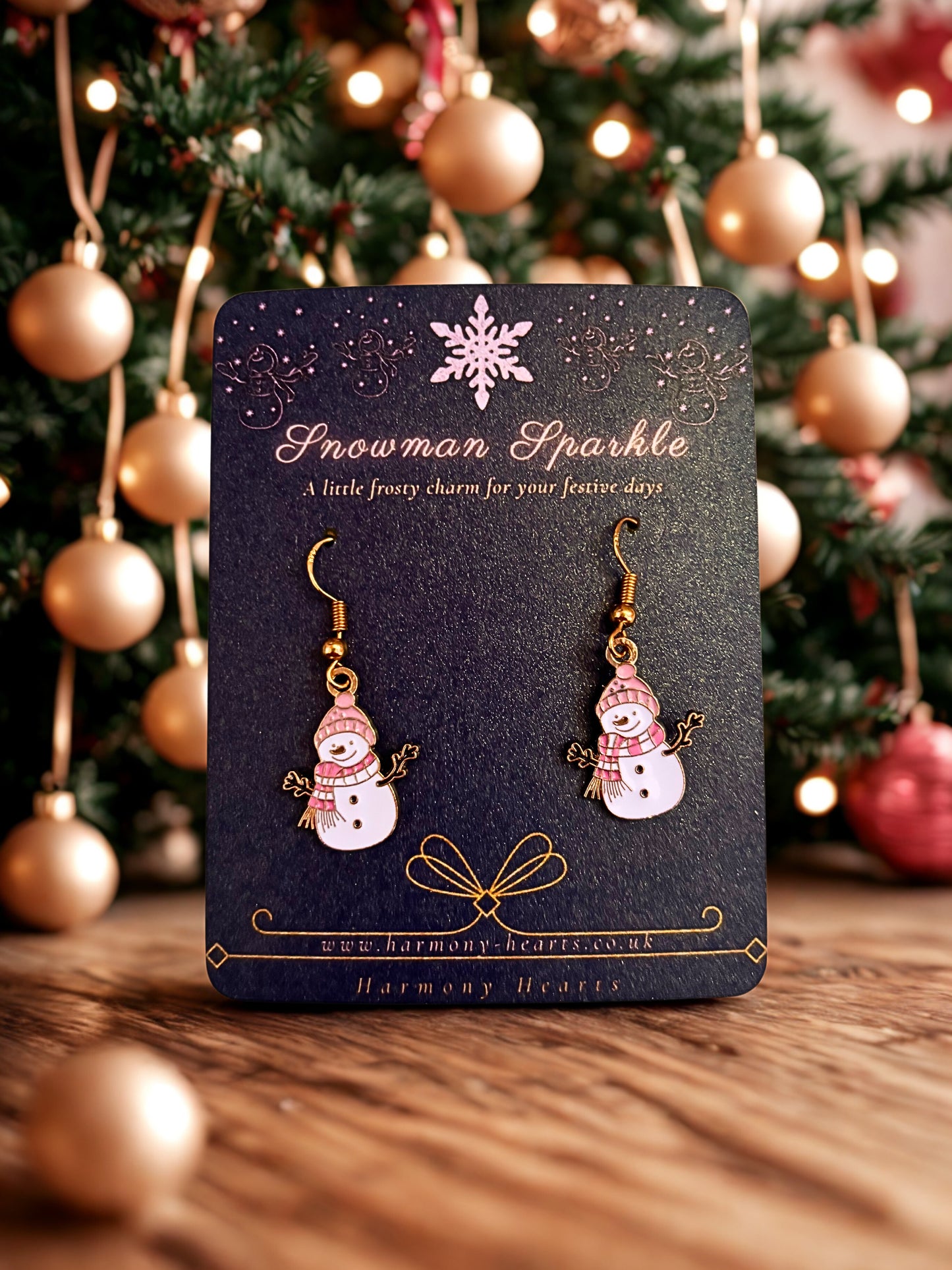 Snowman-themed earrings on a card with a Christmas tree in the background