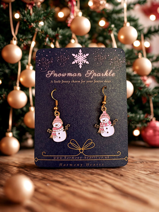 Snowman-themed earrings on a card with a Christmas tree in the background