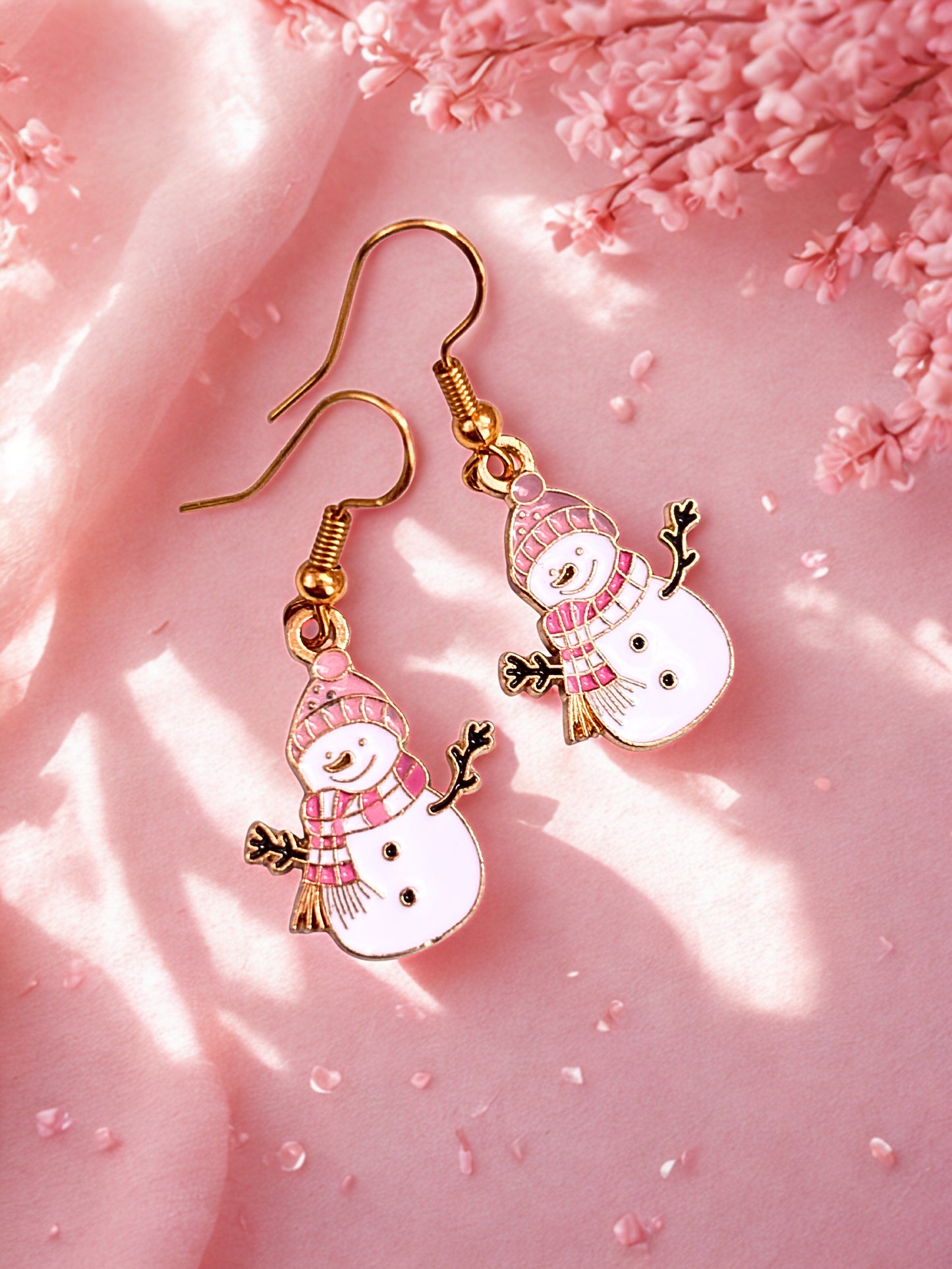 Snowman-themed earrings on a pink background with cherry blossoms