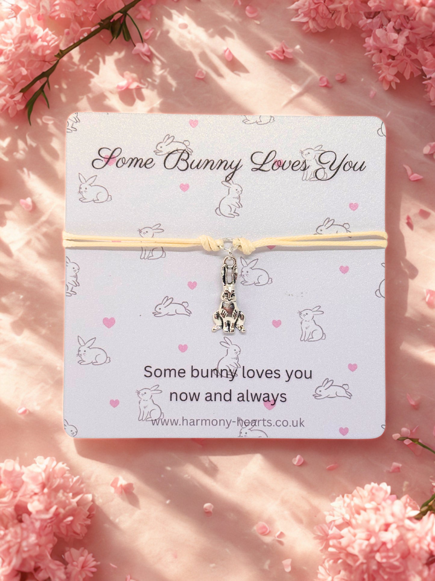 Card with a beige cord bracelet featuring a bunny charm on a pink floral background
